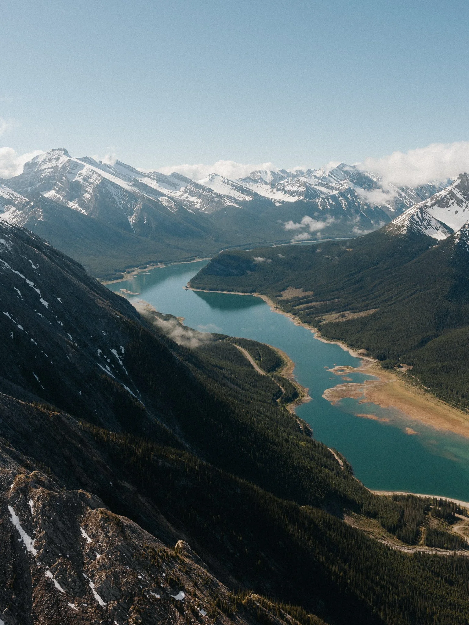 A scenic view of snow-capped mountains, a winding river, and dense forest in a valley.
