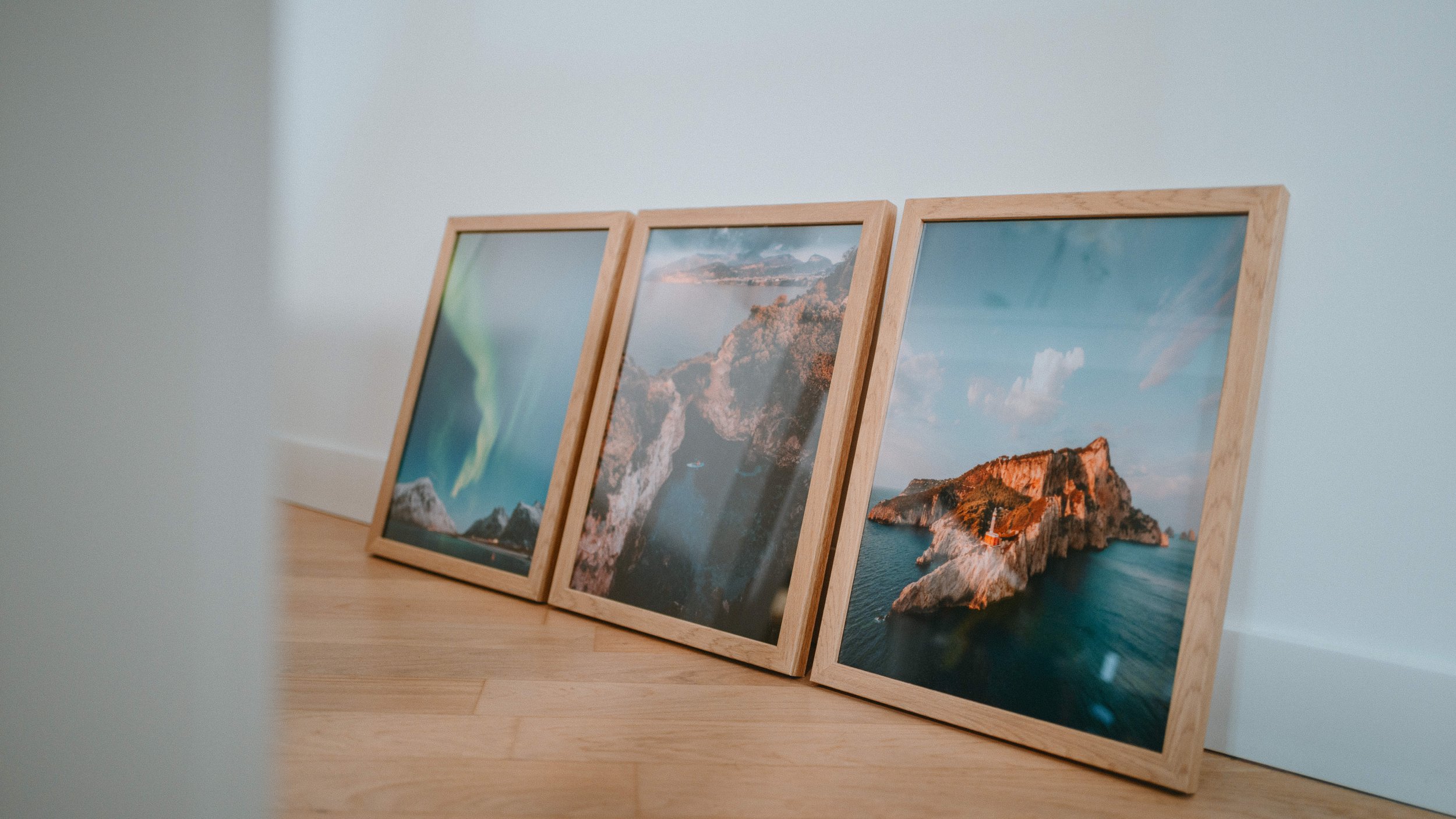Three framed landscape photographs leaning against a wall on a wooden floor.