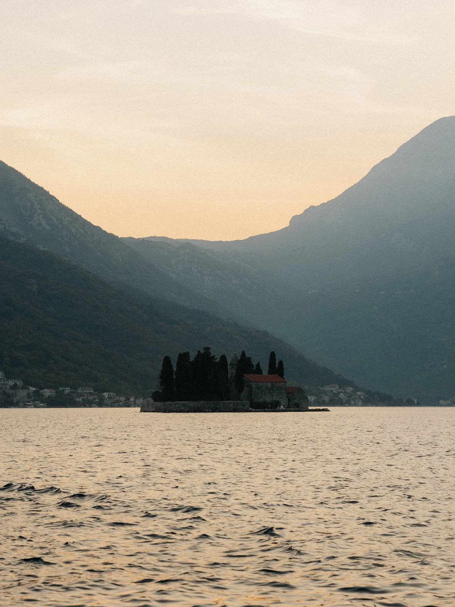 A small island with a church surrounded by water, with mountains in the background at sunset.