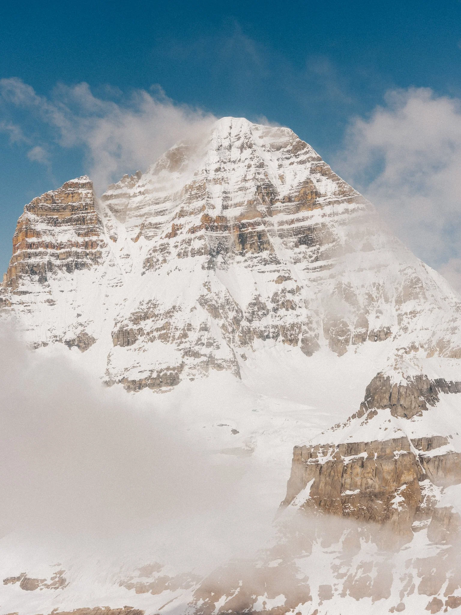 Snow-covered mountain peak with blue sky and wispy clouds.
