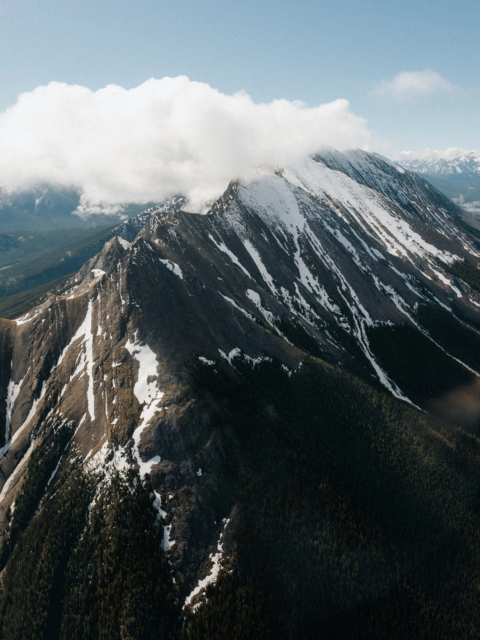 A mountain range with snow-covered peaks, partially obscured by clouds, and dense forested slopes below.