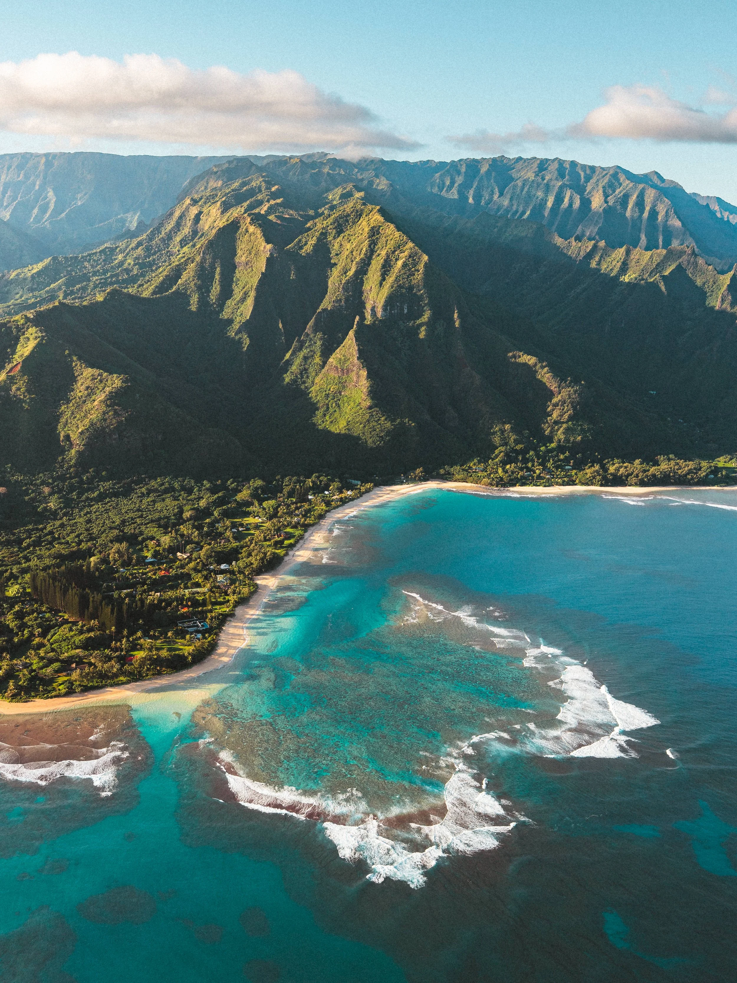 Aerial view of a tropical beach with turquoise water and lush green mountains in the background.