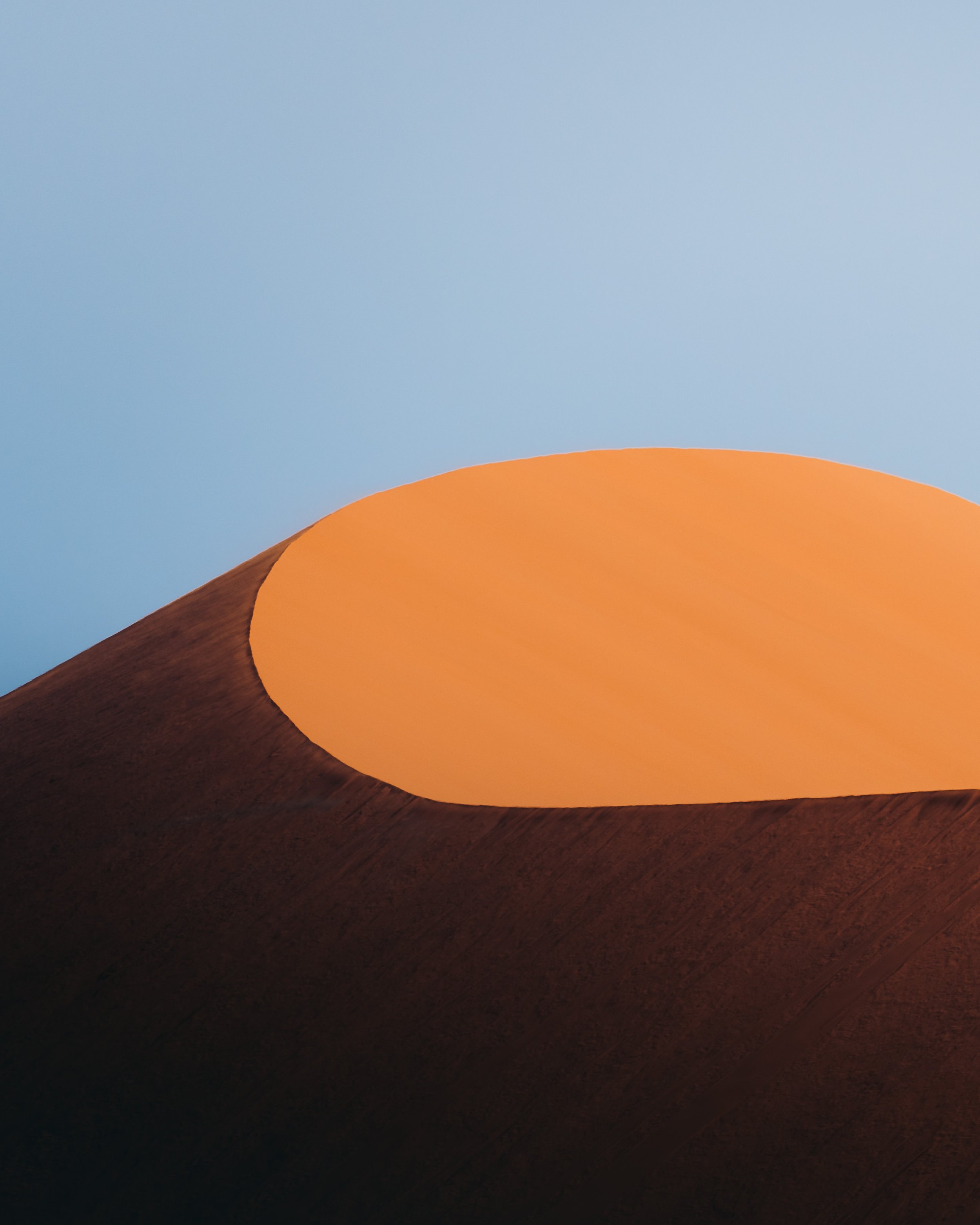 Close-up of a volcanic crater with dark, textured edges and a glowing, smooth orange interior against a clear blue sky.