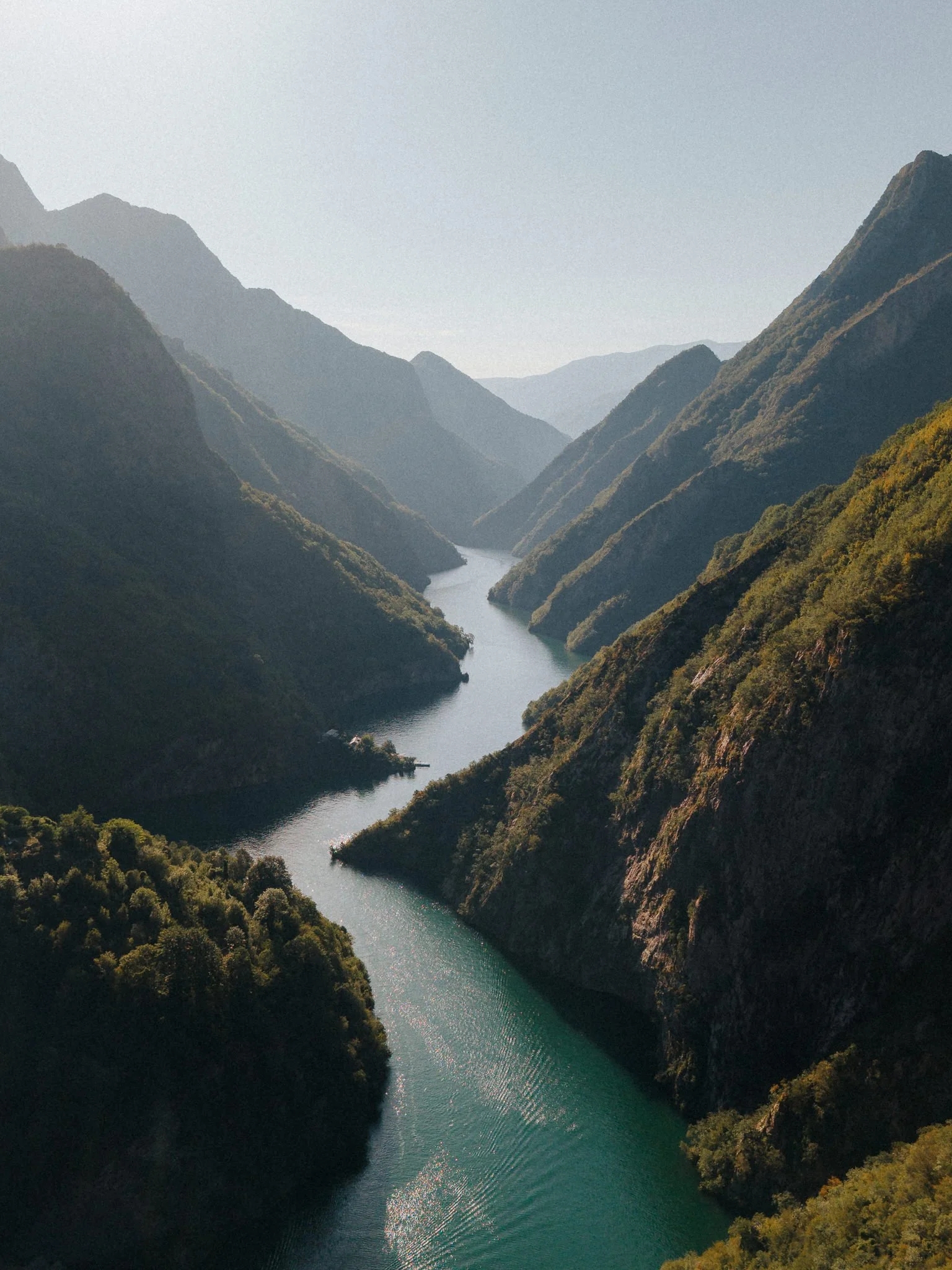 A river running through lush green mountains with a hazy sky.