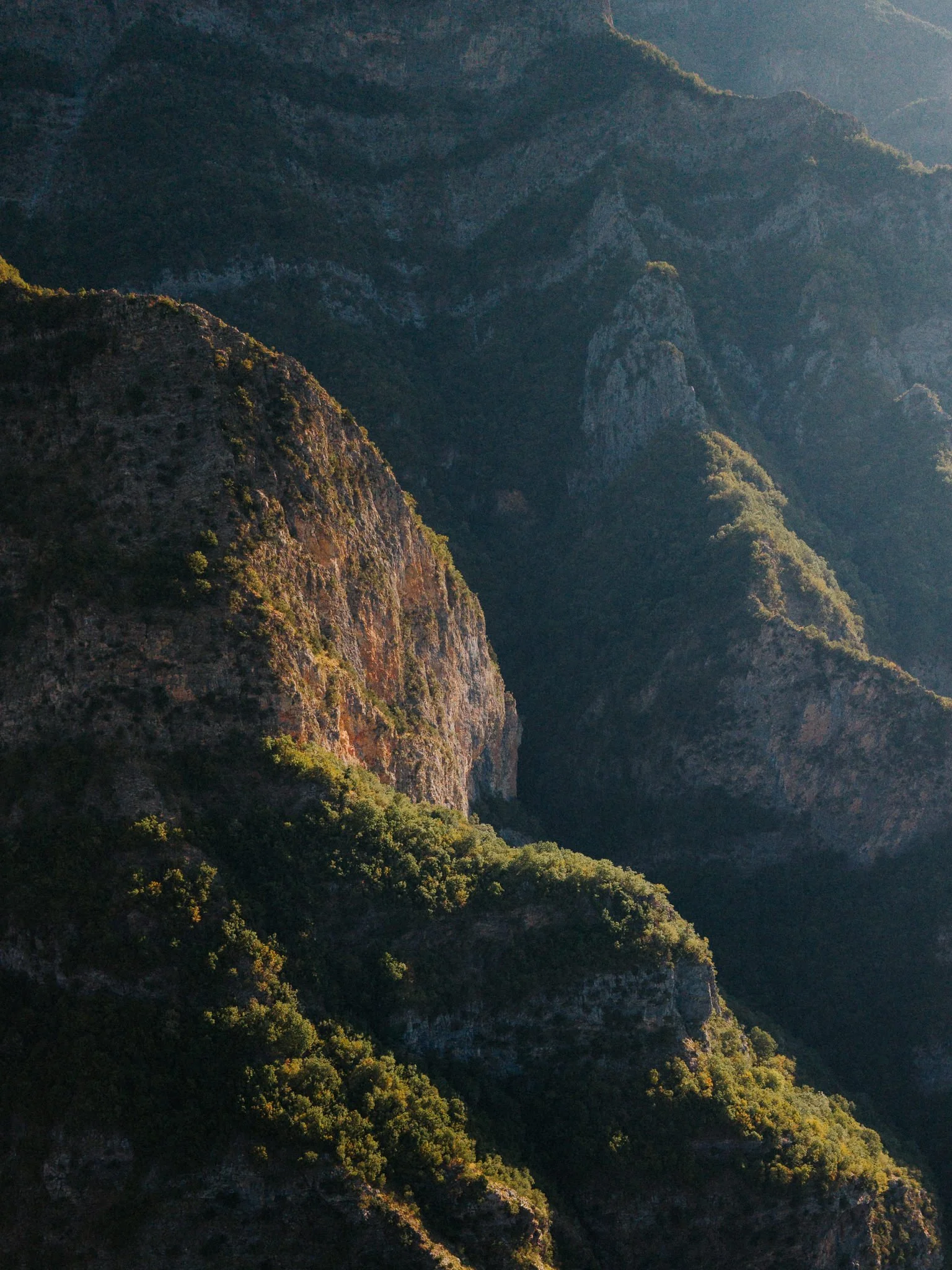 Scenic view of rugged mountain terrain covered in dense green vegetation, with sunlight illuminating parts of the slopes.