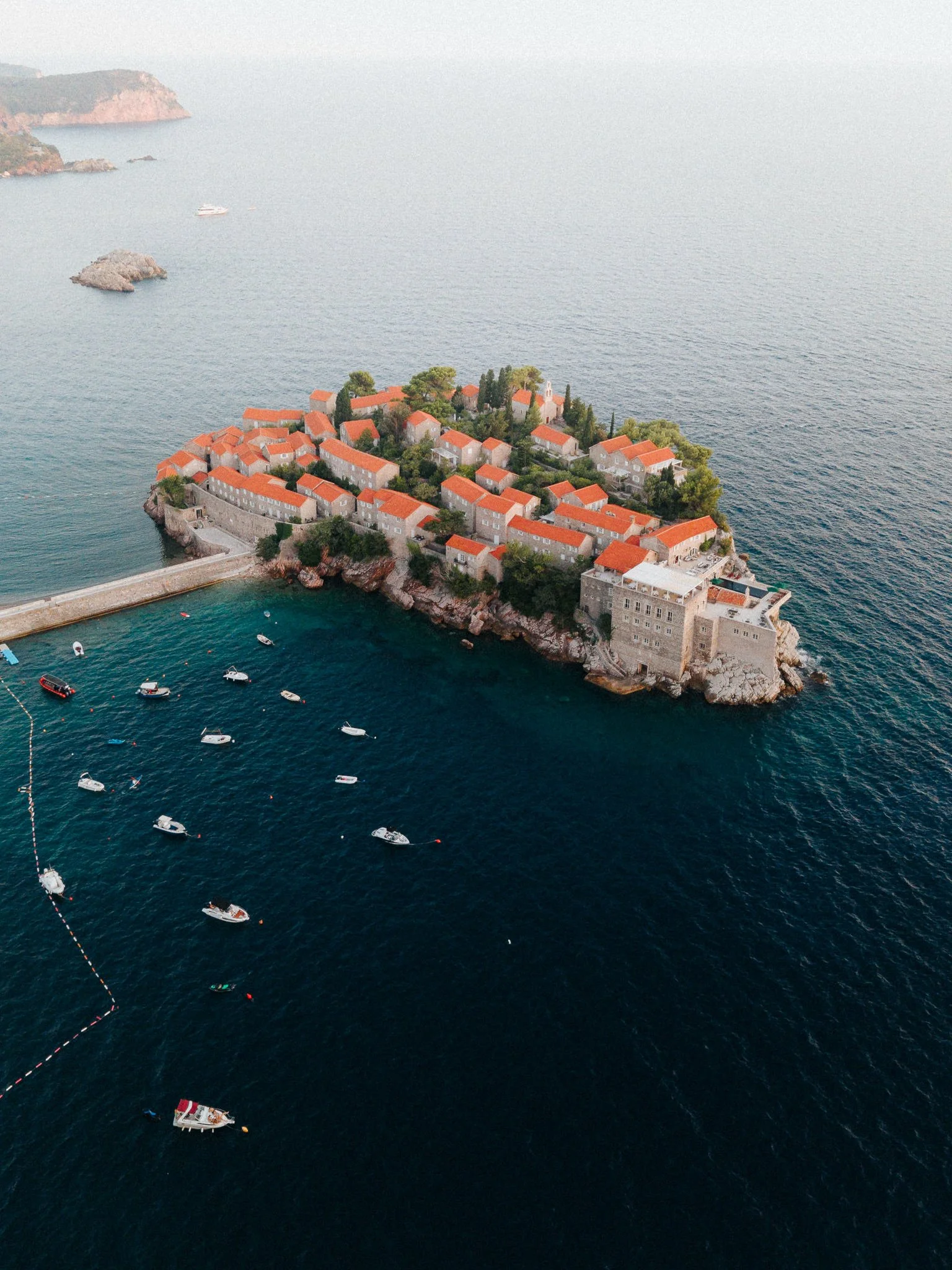 Aerial view of a small Croatian island with red-roofed buildings and boats docked in the surrounding deep blue water.