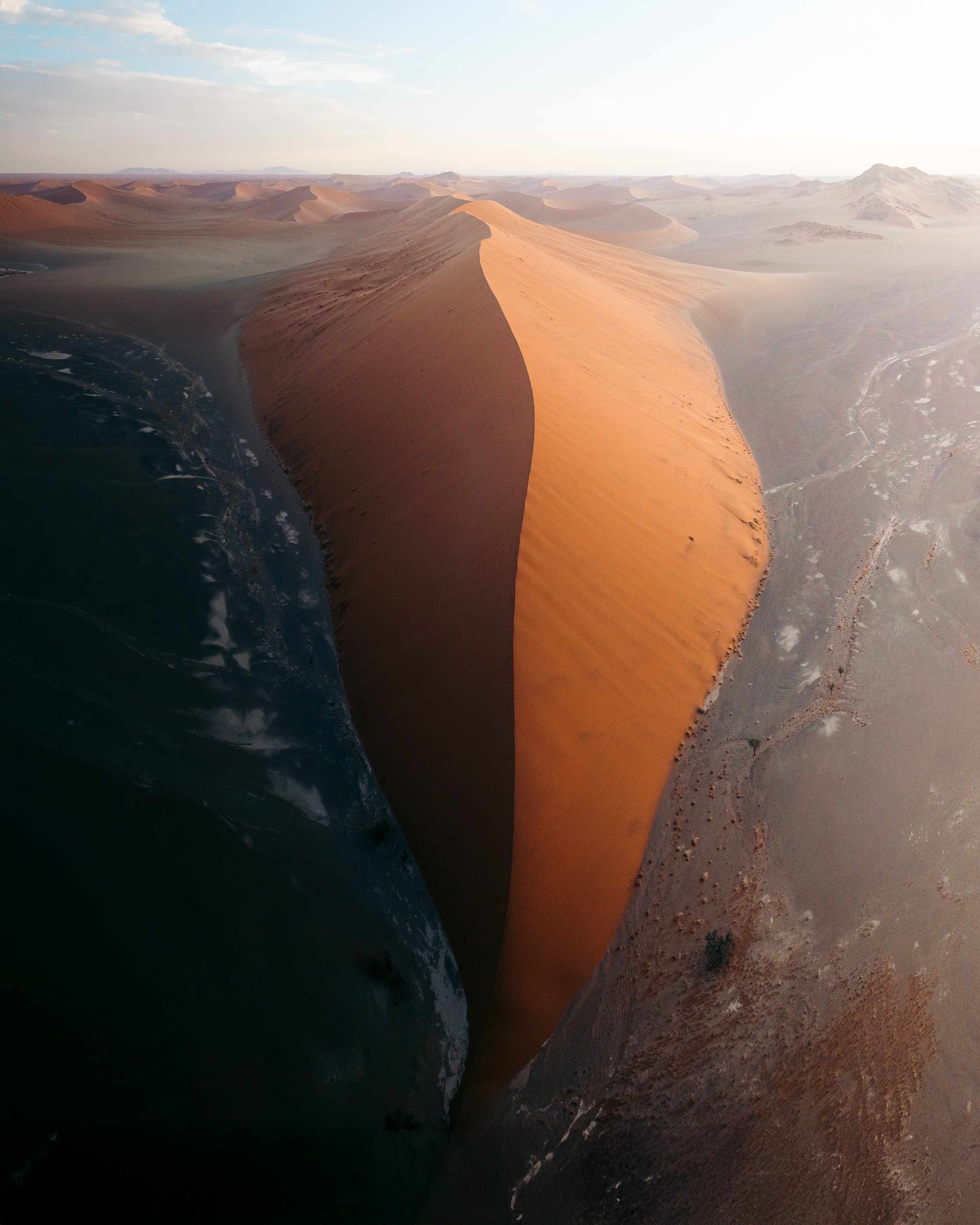 Aerial view of sand dunes in a desert landscape with a clear sky in the background.