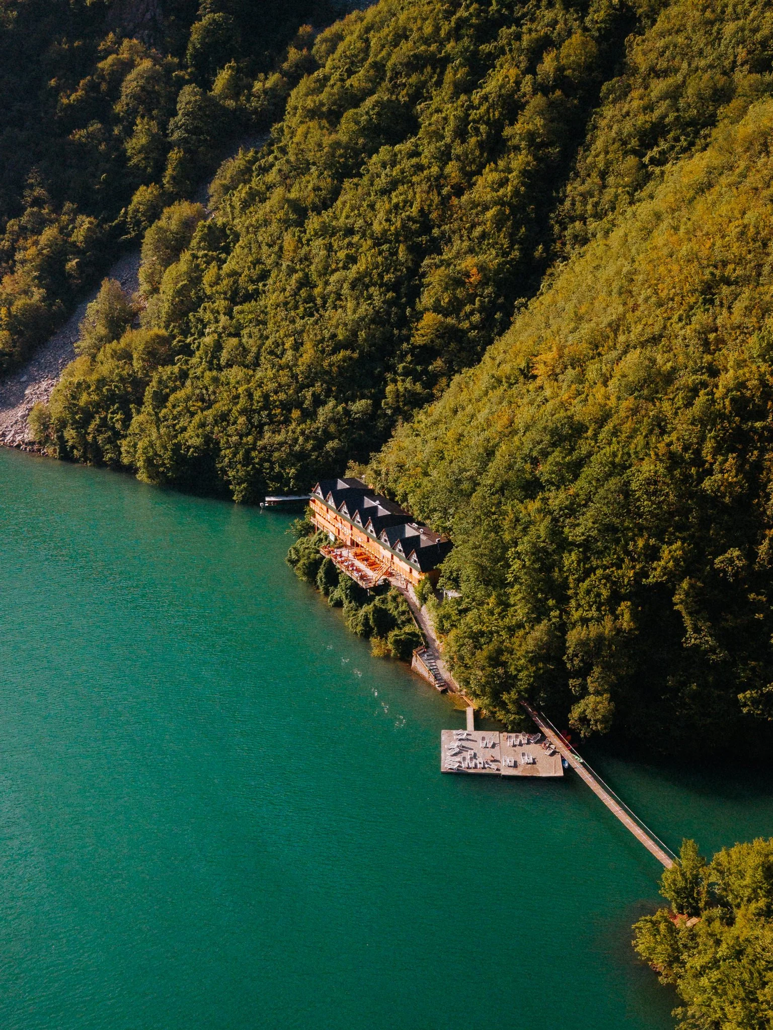 Aerial view of a lake surrounded by forested hills with a building and dock along the shoreline.