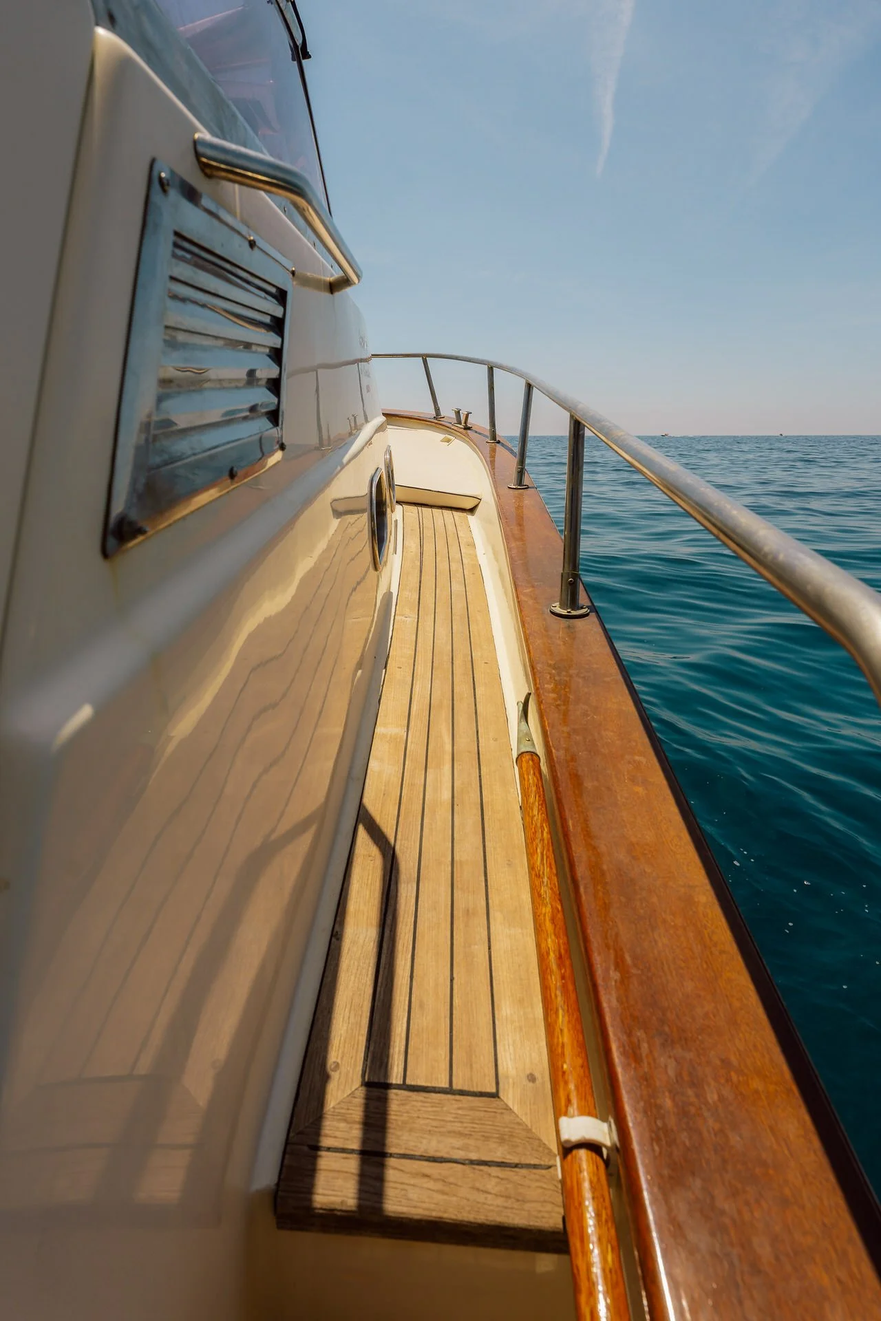 View from a boat deck showing a wooden surface, metal railing, blue ocean, and clear sky.