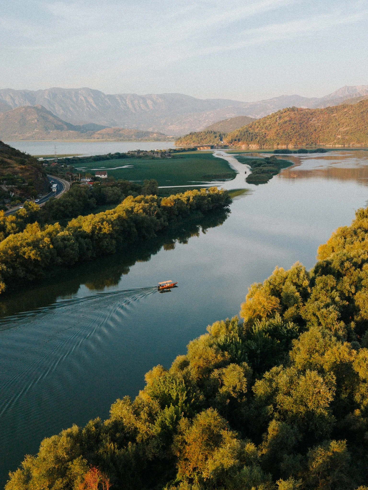 A river winding through a landscape with green trees, mountains in the background, and a boat on the water.