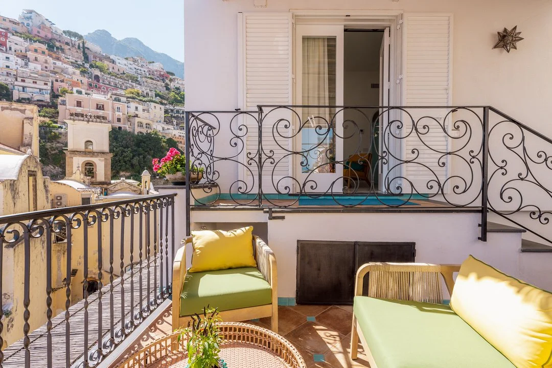 Balcony with outdoor seating and view of hillside houses in a Mediterranean town.
