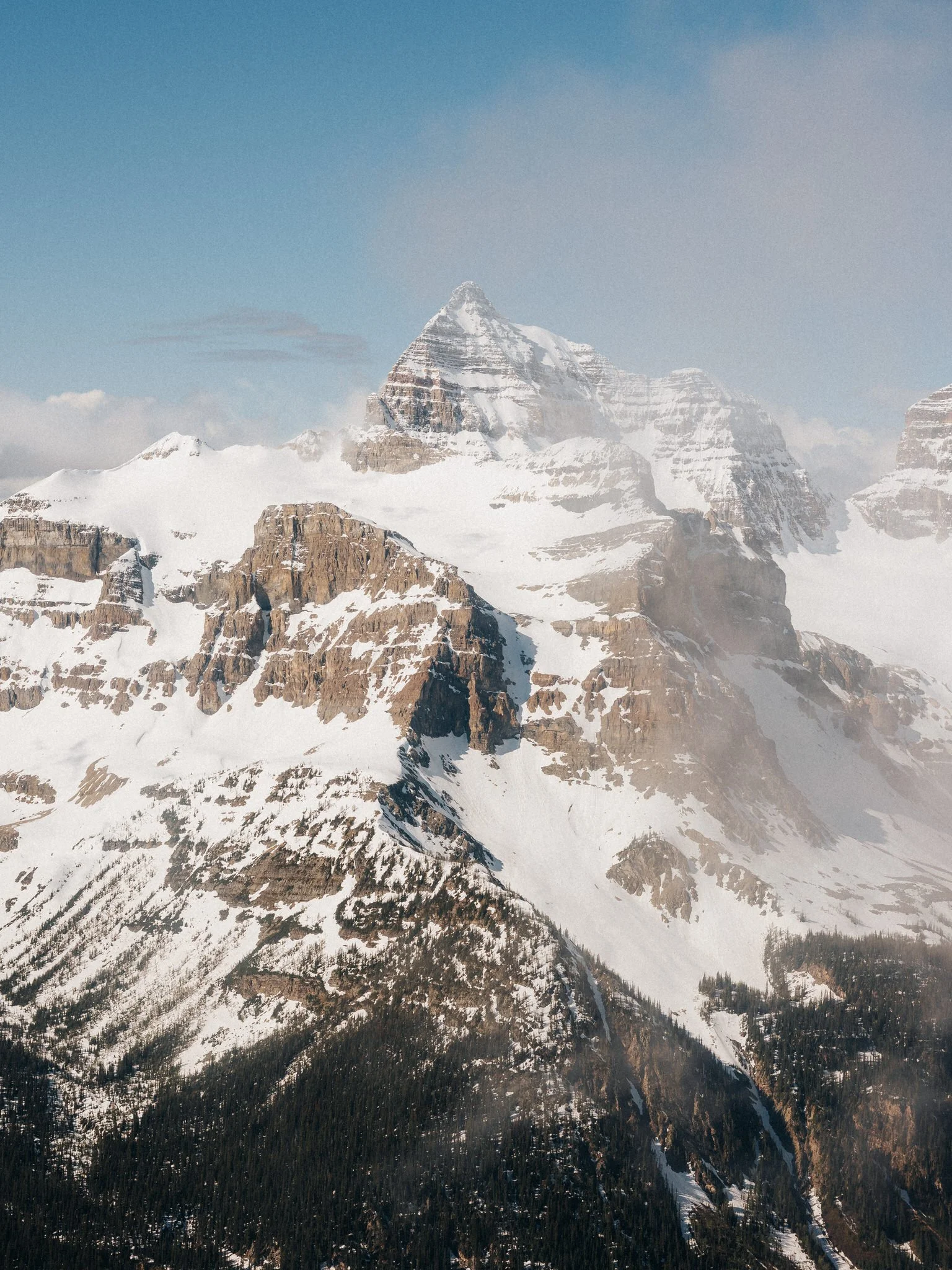Snow-covered mountain peaks under a partly cloudy sky with a snowy slope below.