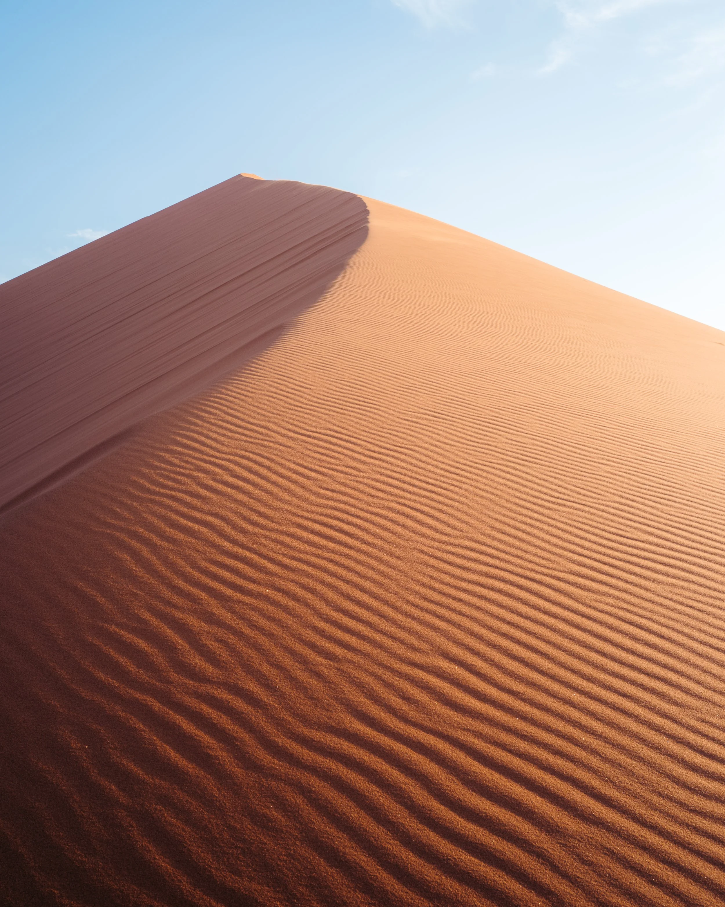 Close-up of a desert sand dune with ripples, under a clear blue sky.