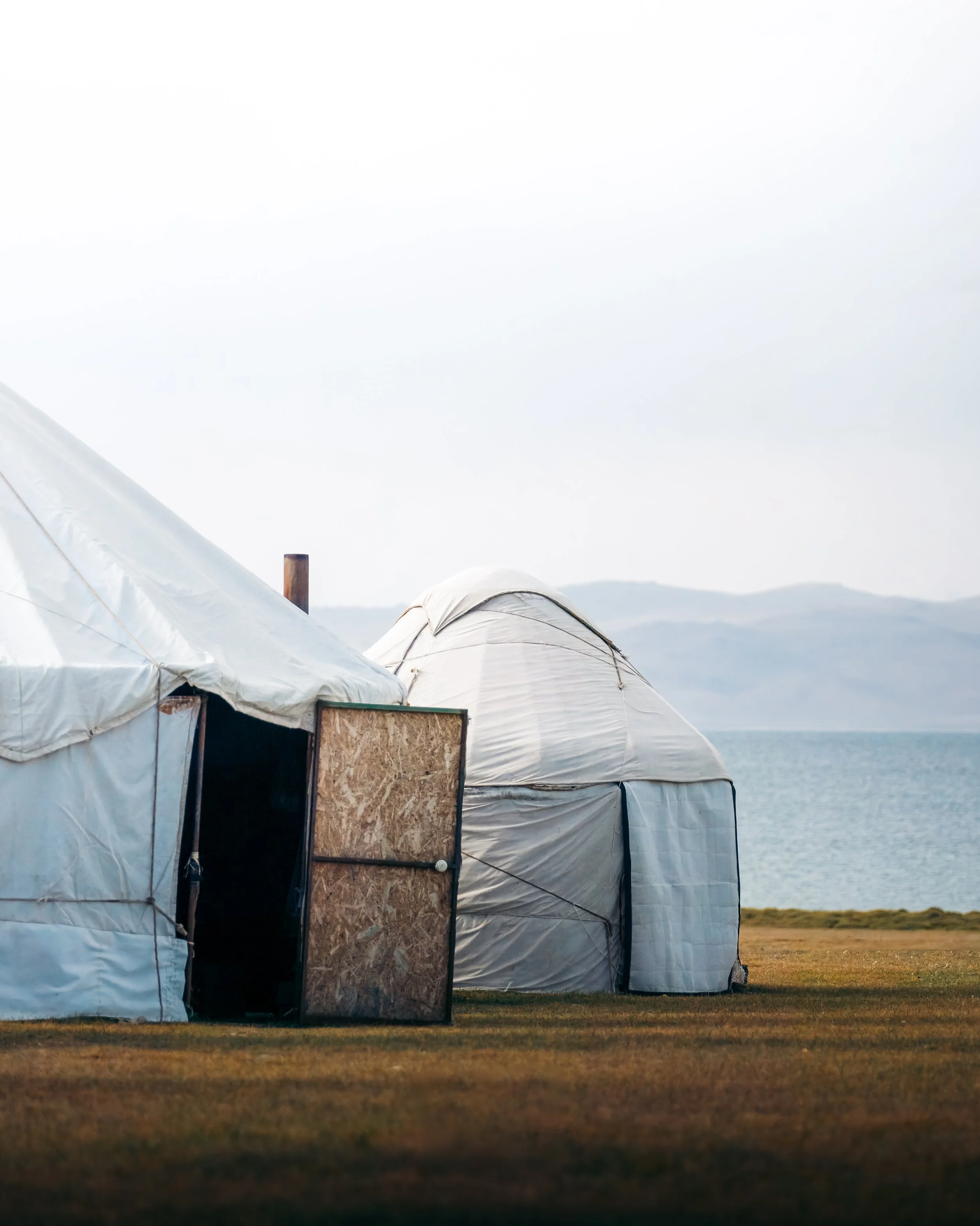 White tents on grassy terrain near water with mountains in the background.