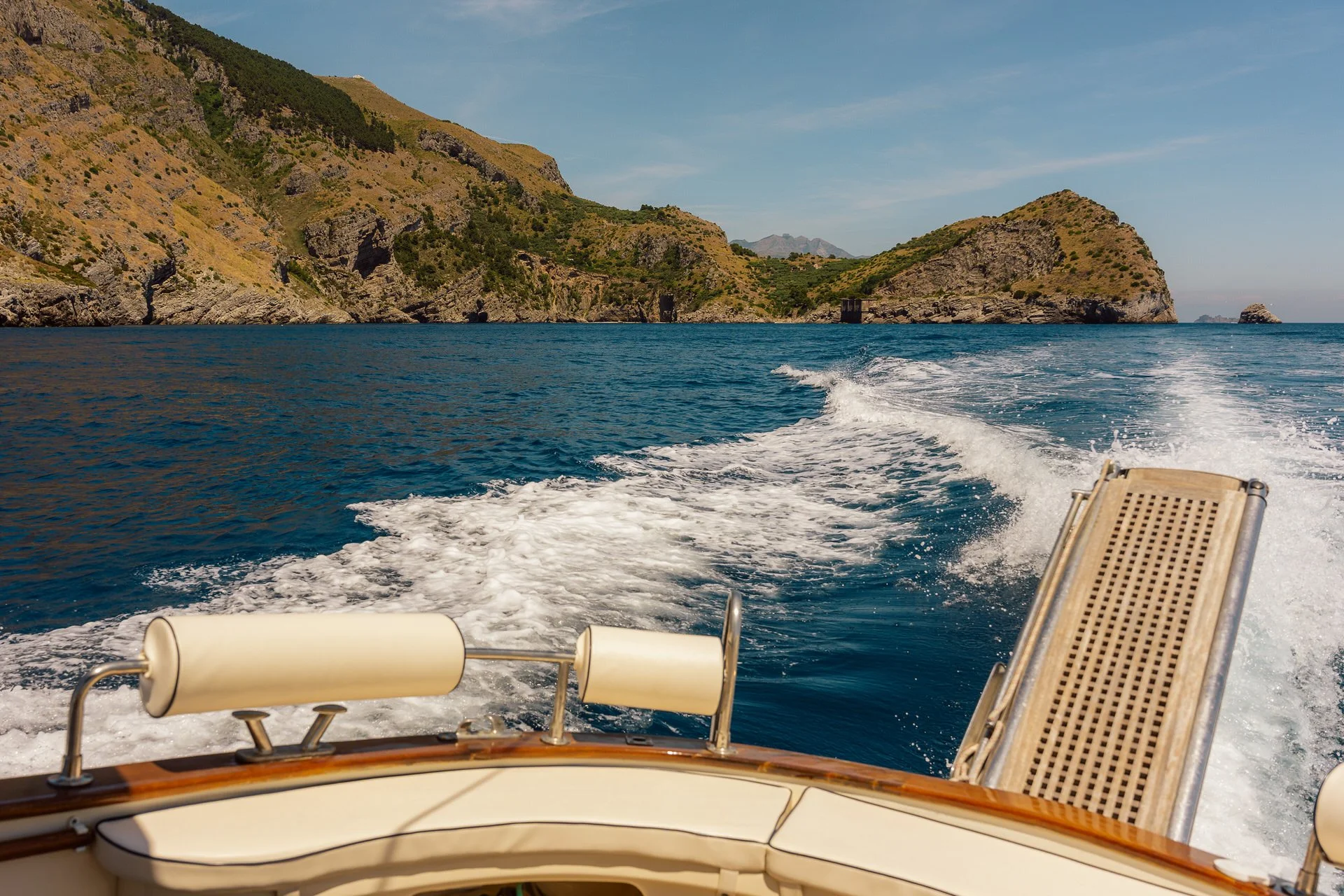 View from a boat showing the wake on the water and a hillside in the distance.