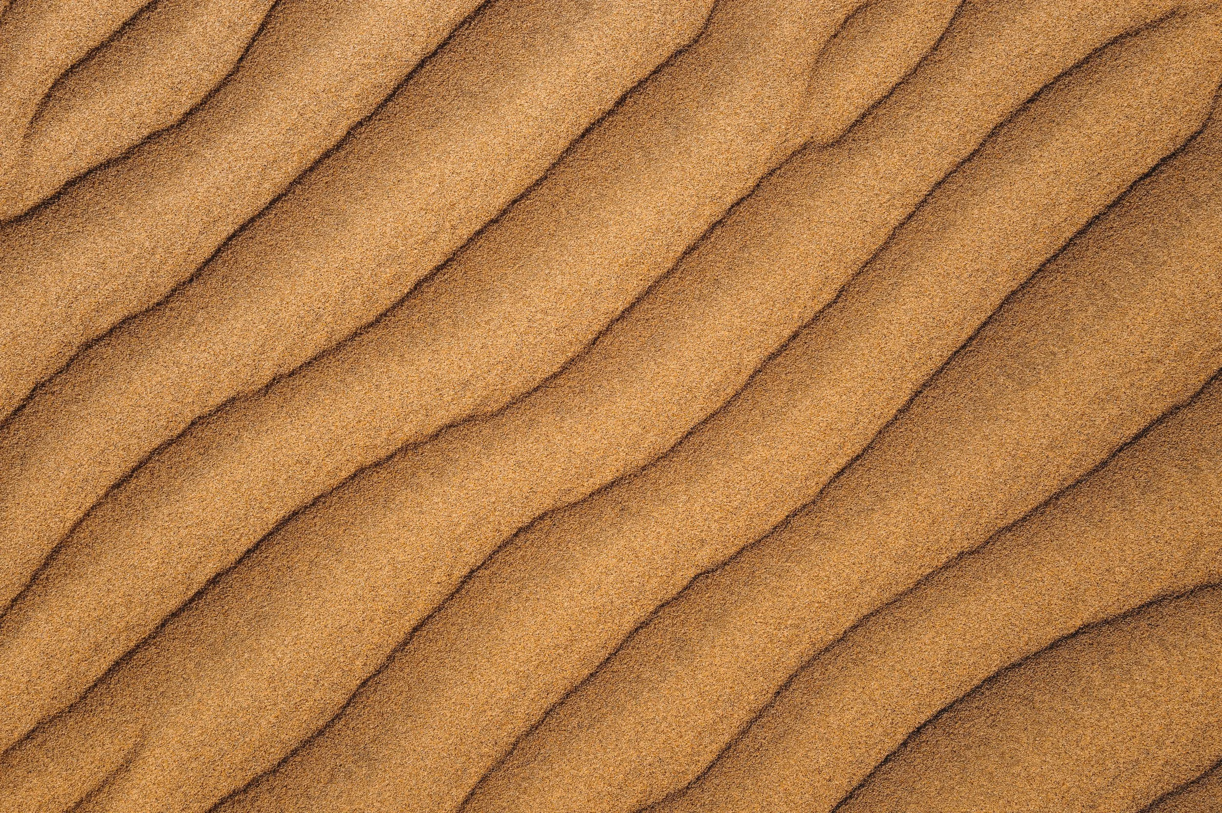 Close-up of sand dunes with wavy patterns and shadows.