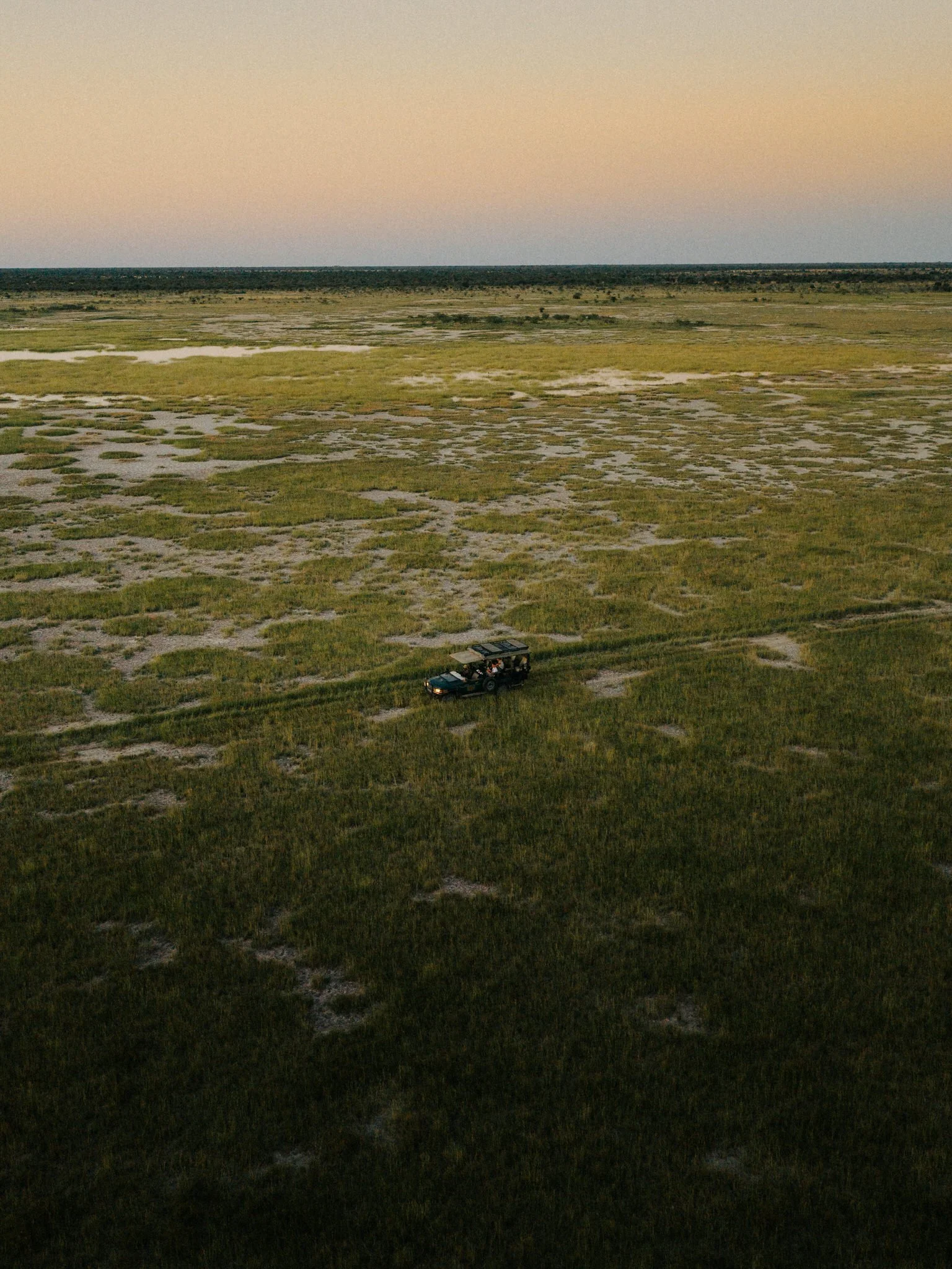 A landscape view of a flat, grassy marshland during sunset, with a vehicle in the foreground and a broad sky above.