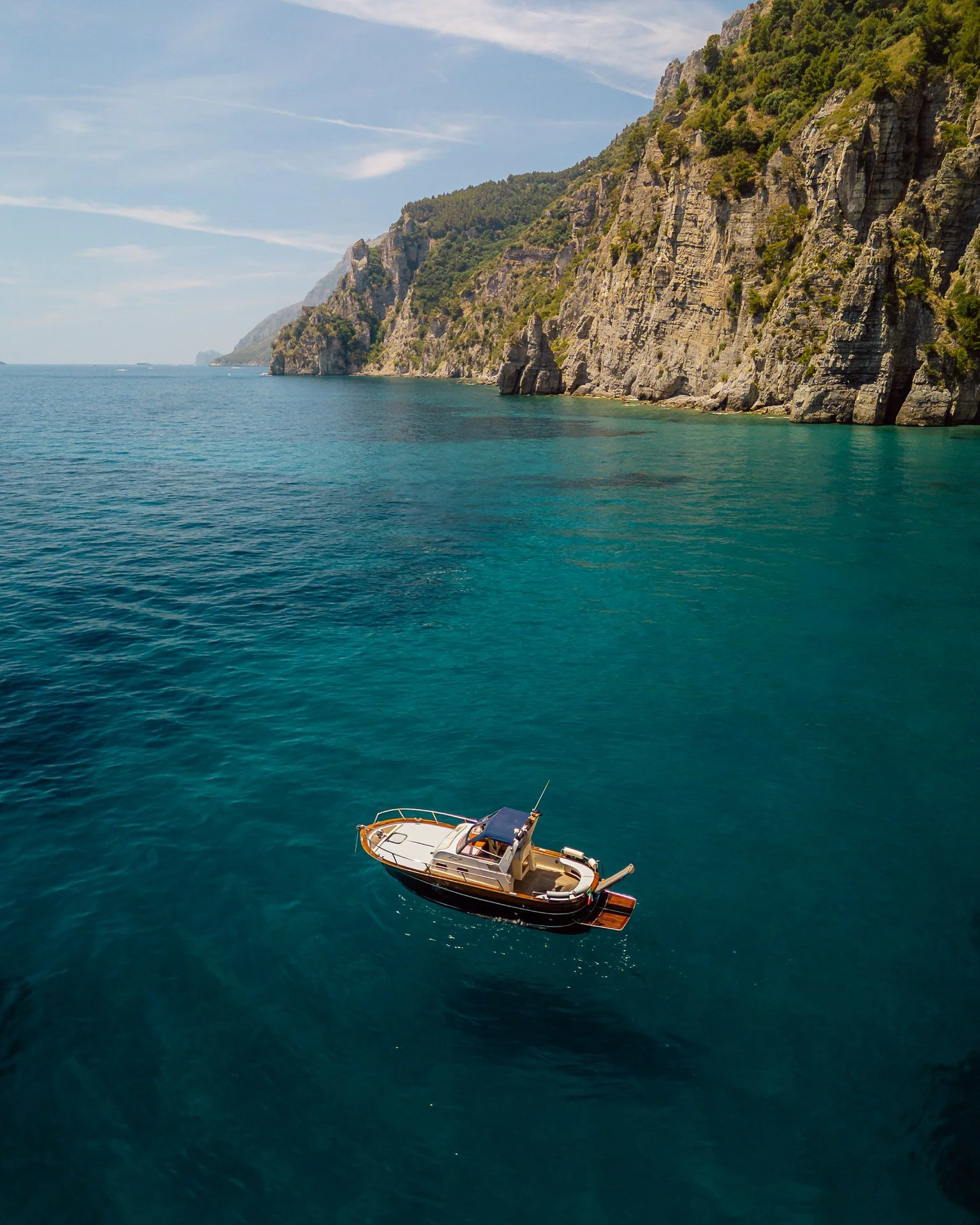 A boat floating on calm ocean water near a rugged cliffside with green vegetation under a blue sky.