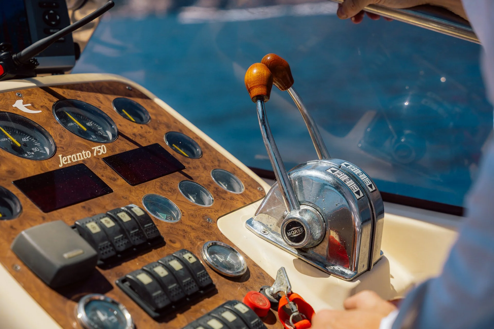 Close-up of a boat’s control panel with gauges and a throttle lever labeled "MORSE". The panel has a wood finish with various dials and switches, and a person’s hand is seen adjusting the throttle.