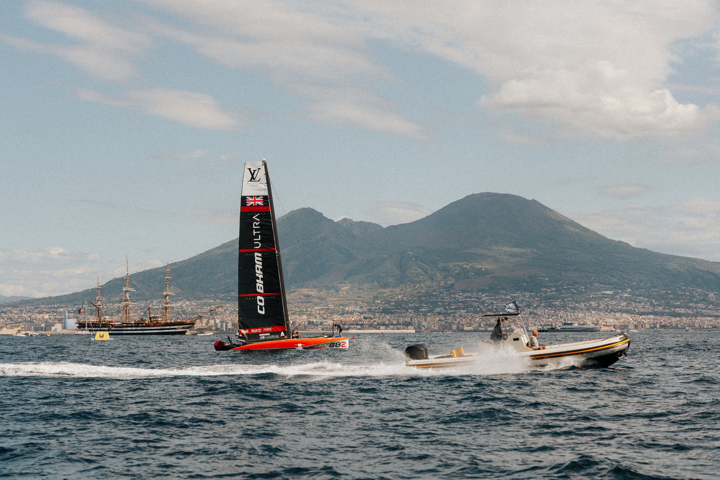 Boats racing on the water with a city and mountains in the background.