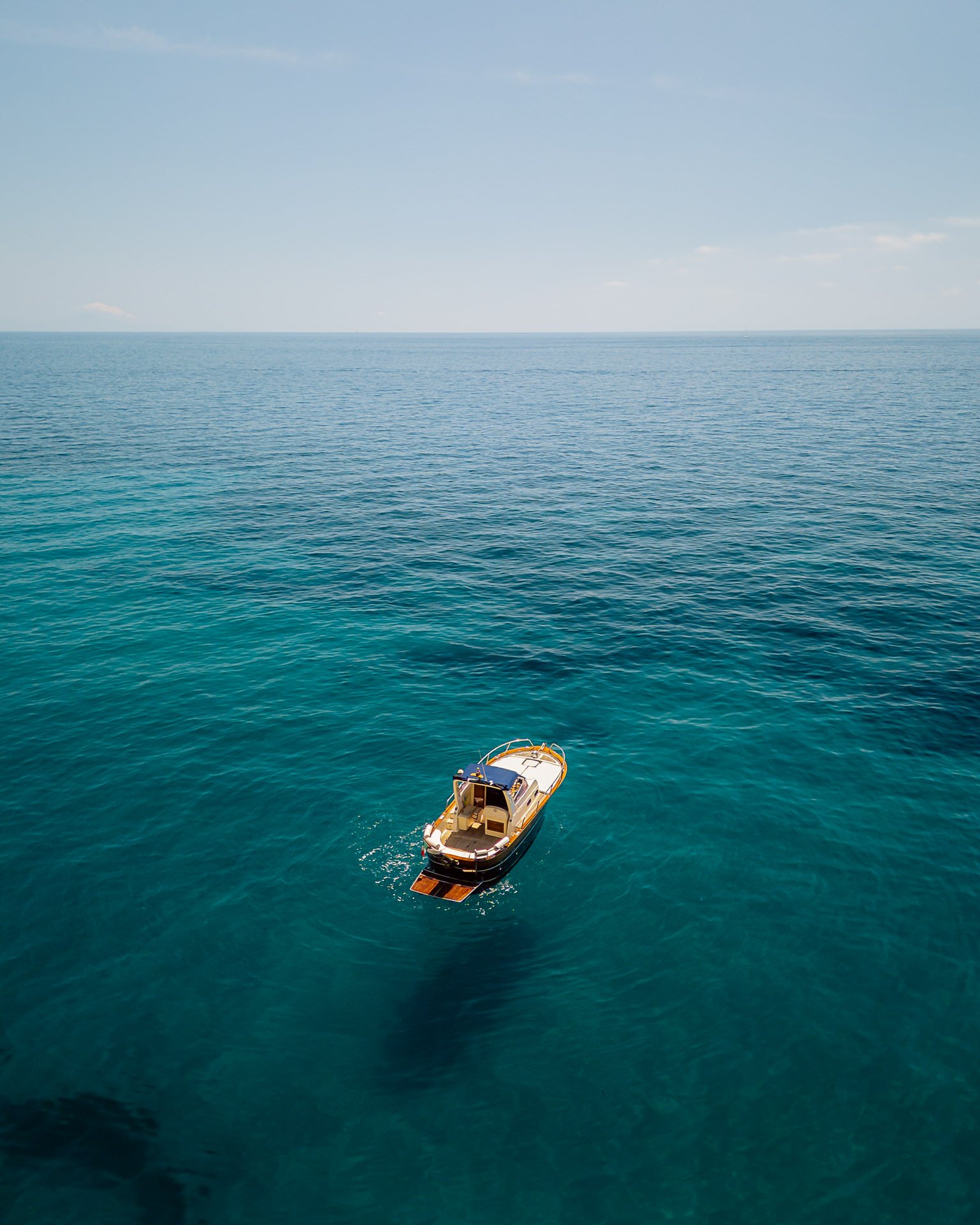 A boat floating on calm blue-green ocean water under a clear sky.