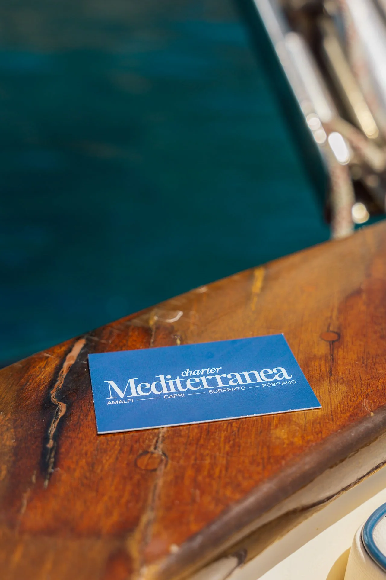 Blue business card for Charter Mediterranea resting on a wooden surface.