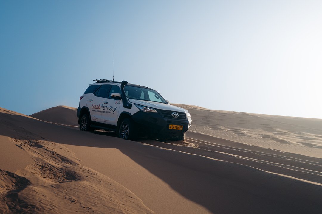 A white SUV with advertisement on its side, parked on sand dunes in a desert landscape.