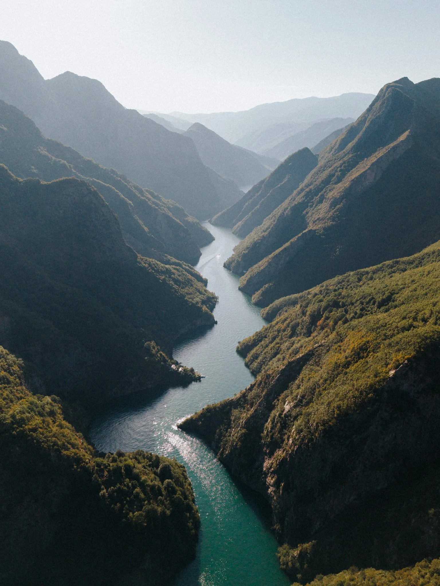 Aerial view of a river winding through a deep valley surrounded by steep, forested mountains.