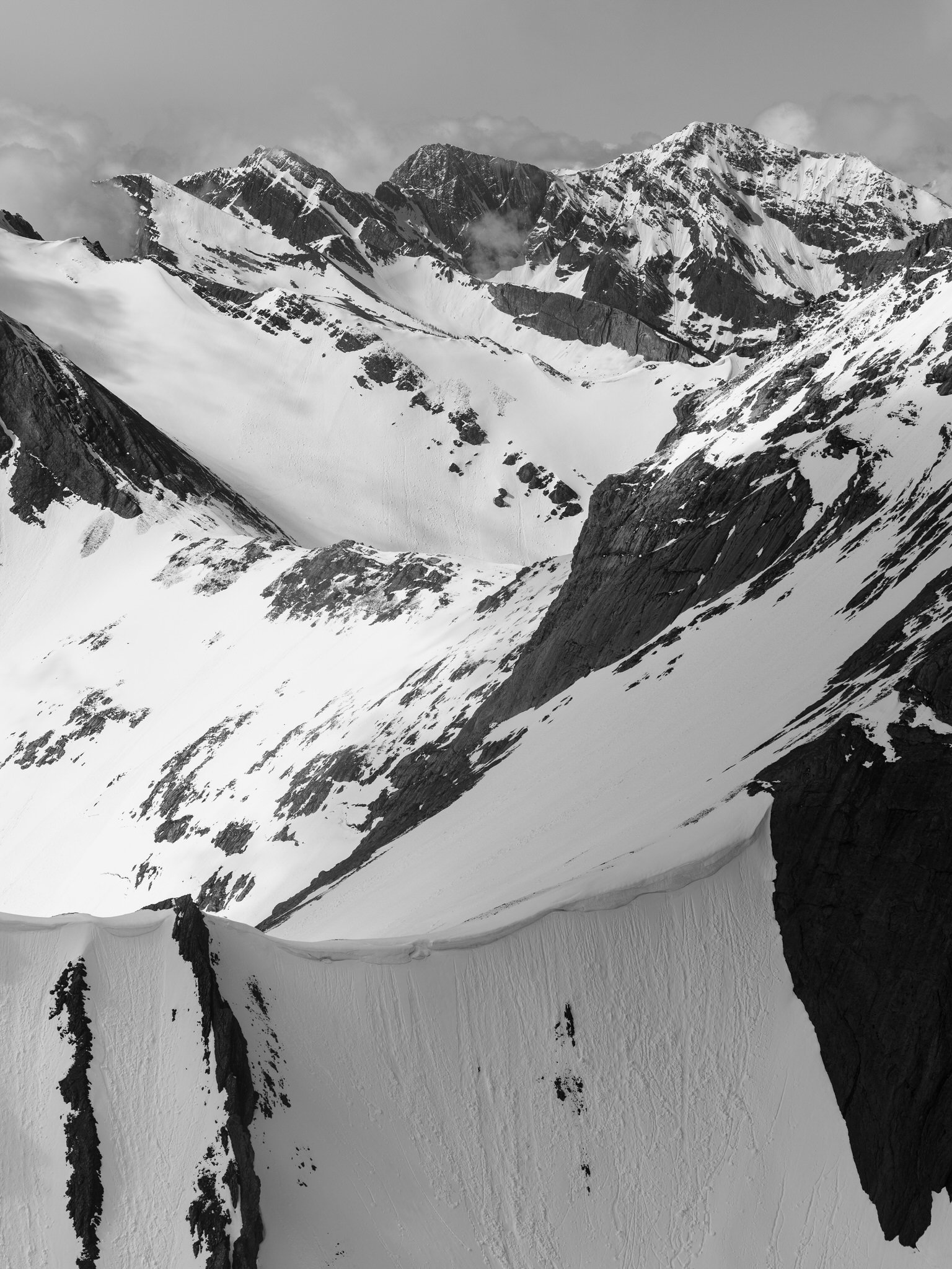 Snow-covered mountain peaks with dark rocky slopes, in black and white.