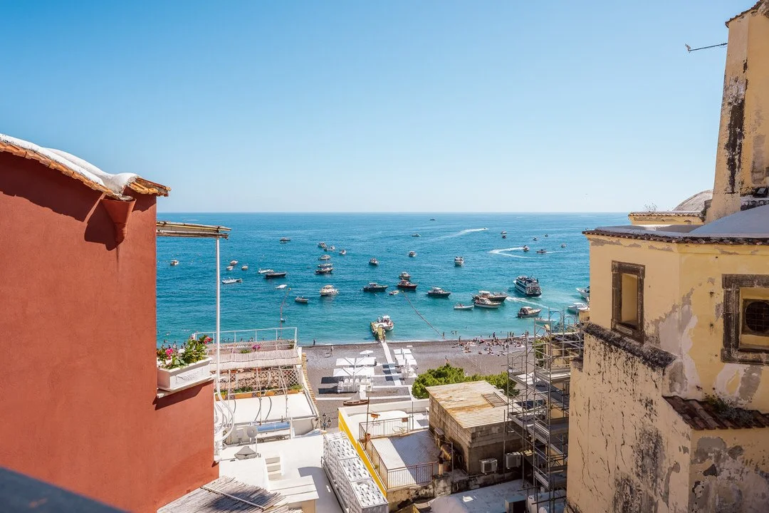 View of a harbor with boats, seen from between colorful buildings on a sunny day.