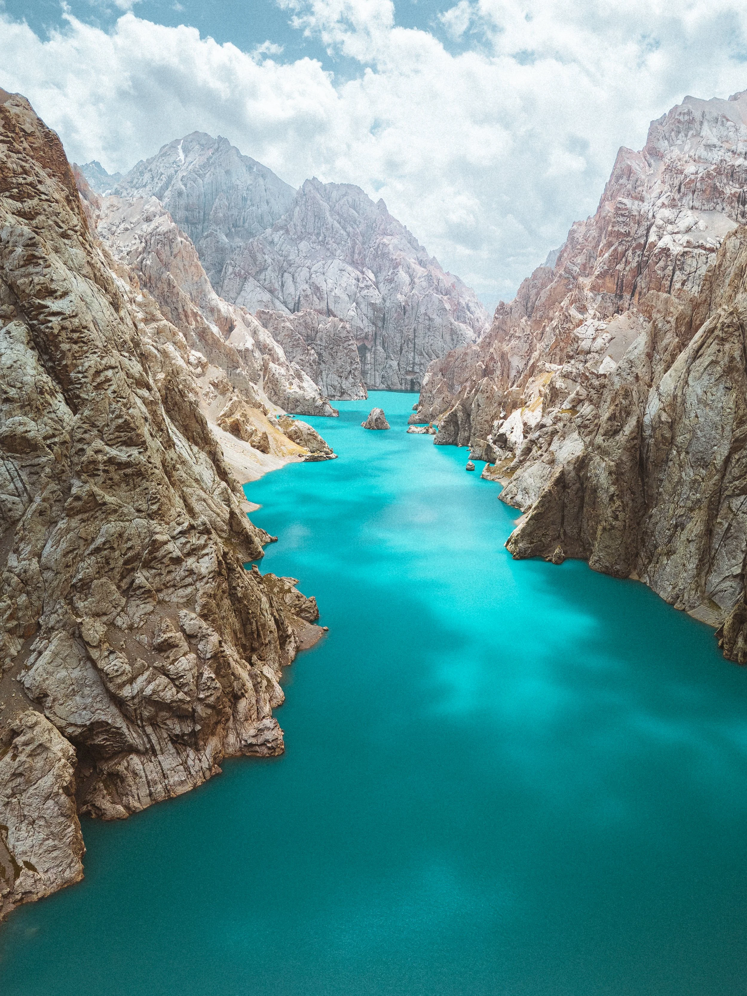 A reservoir with blue water surrounded by rocky, mountainous cliffs and partly cloudy sky.