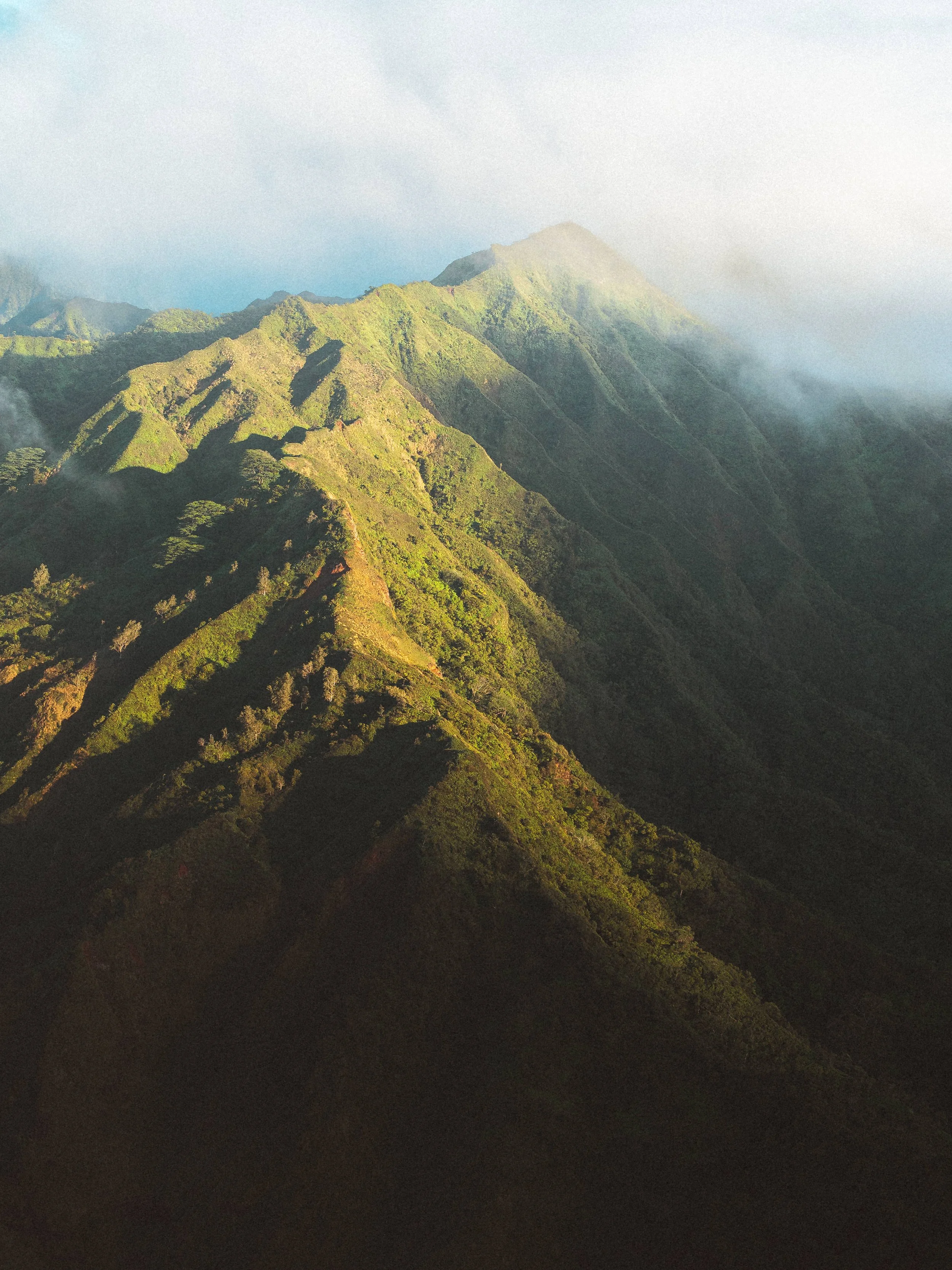 Aerial view of lush green mountains with clouds around them.