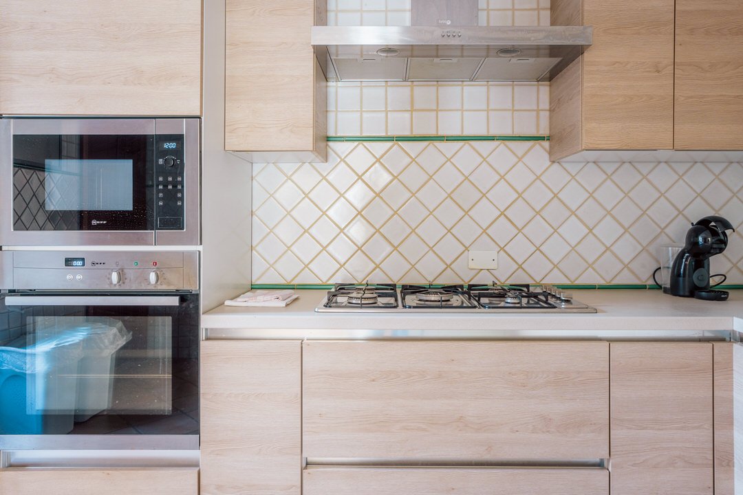 Modern kitchen with built-in microwave and oven, gas cooktop, wall-mounted range hood, coffee maker on the countertop, and beige wood cabinets.