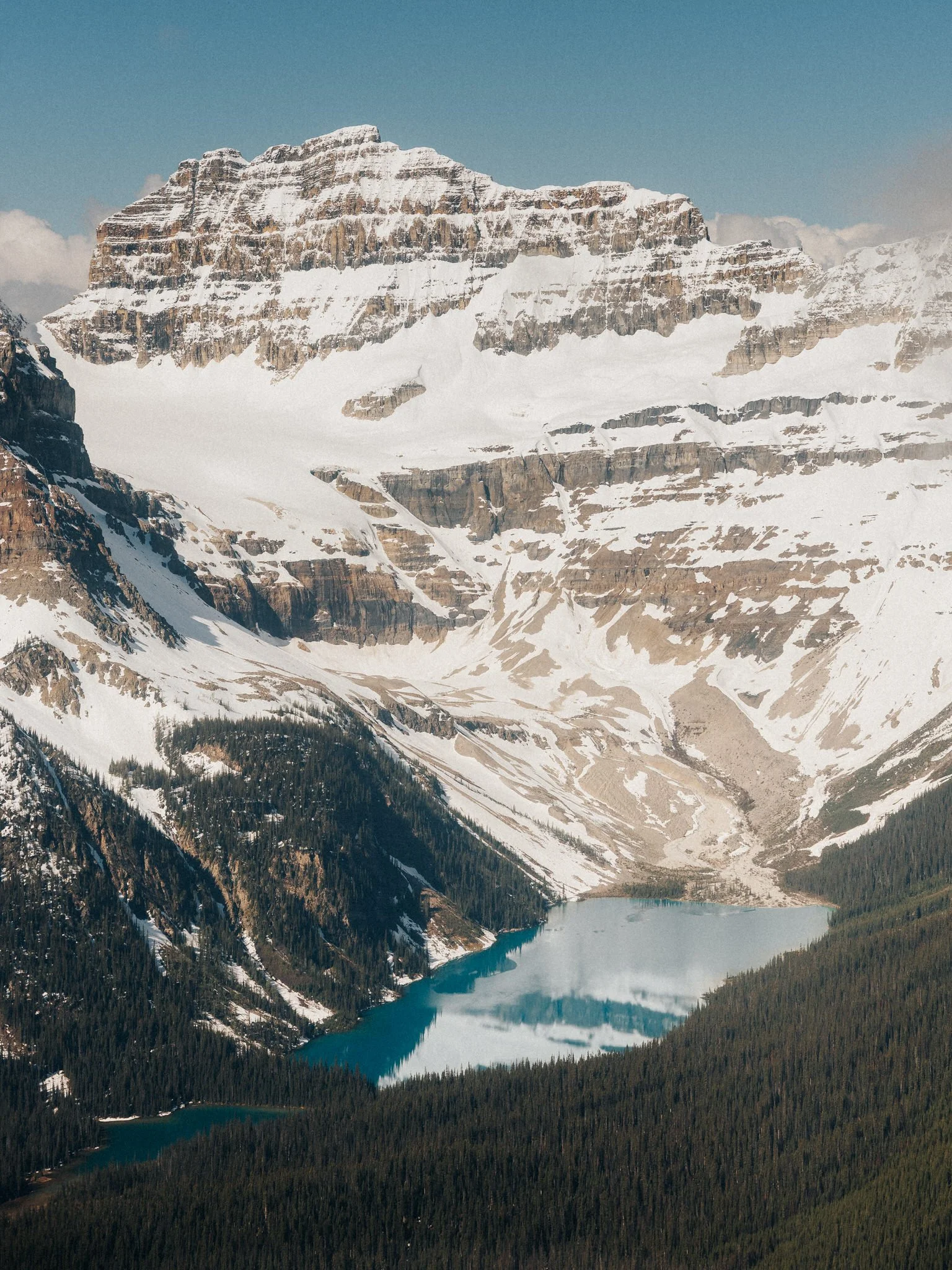 Snow-capped mountain peaks above a forested landscape with a turquoise lake at the base.