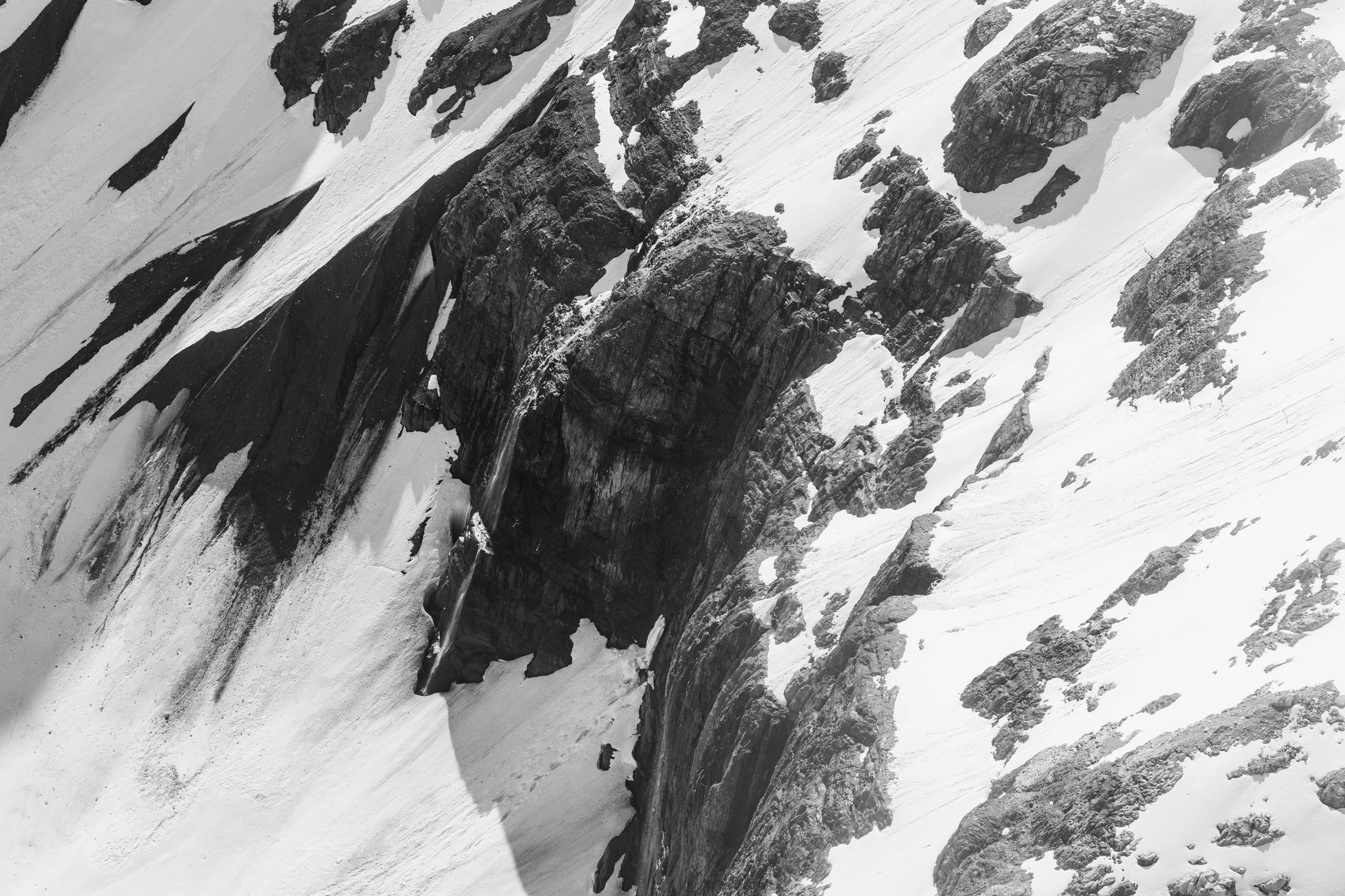 Black and white photograph of a rugged, snow-covered mountain with steep rocky cliffs and ridges.