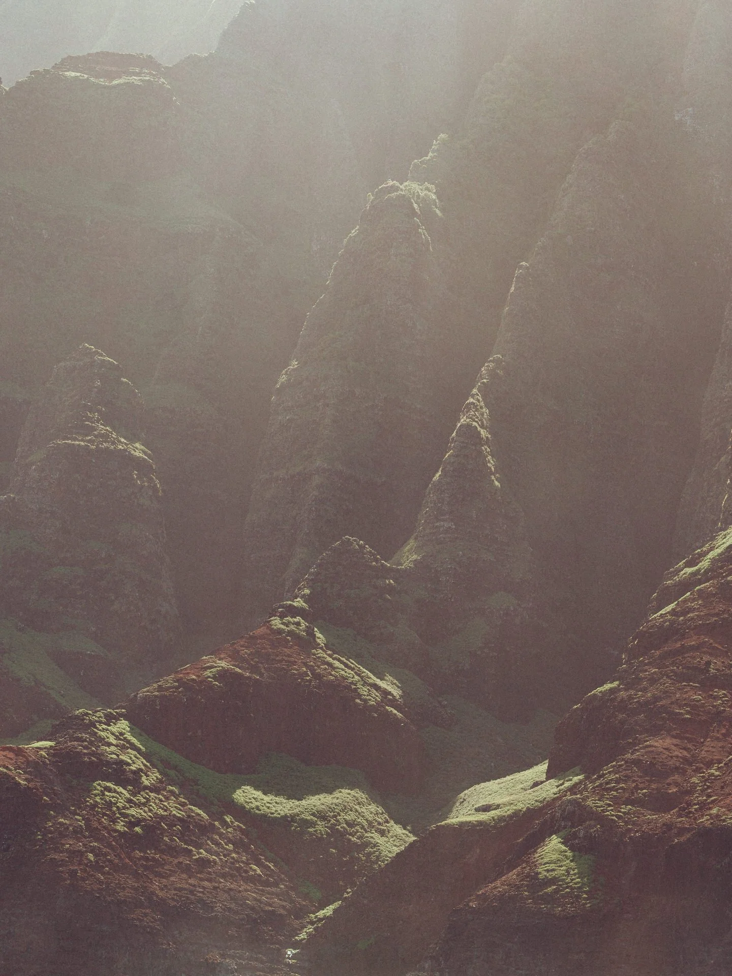Mountain peaks with steep slopes covered in moss and greenery, shrouded in mist