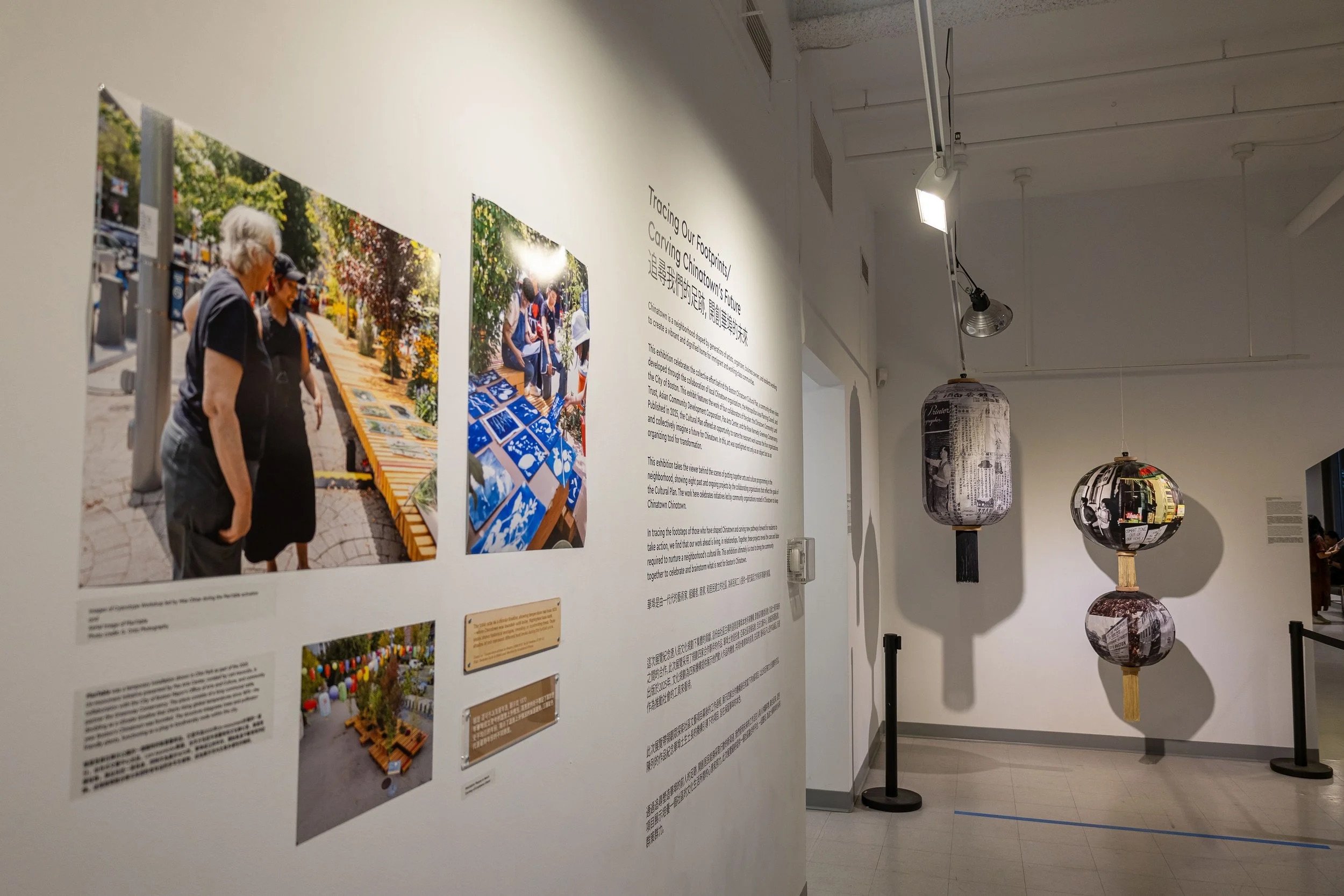 Exhibition wall with photographs and text describing Chinatown's community and future, with hanging paper lanterns in an art gallery setting.