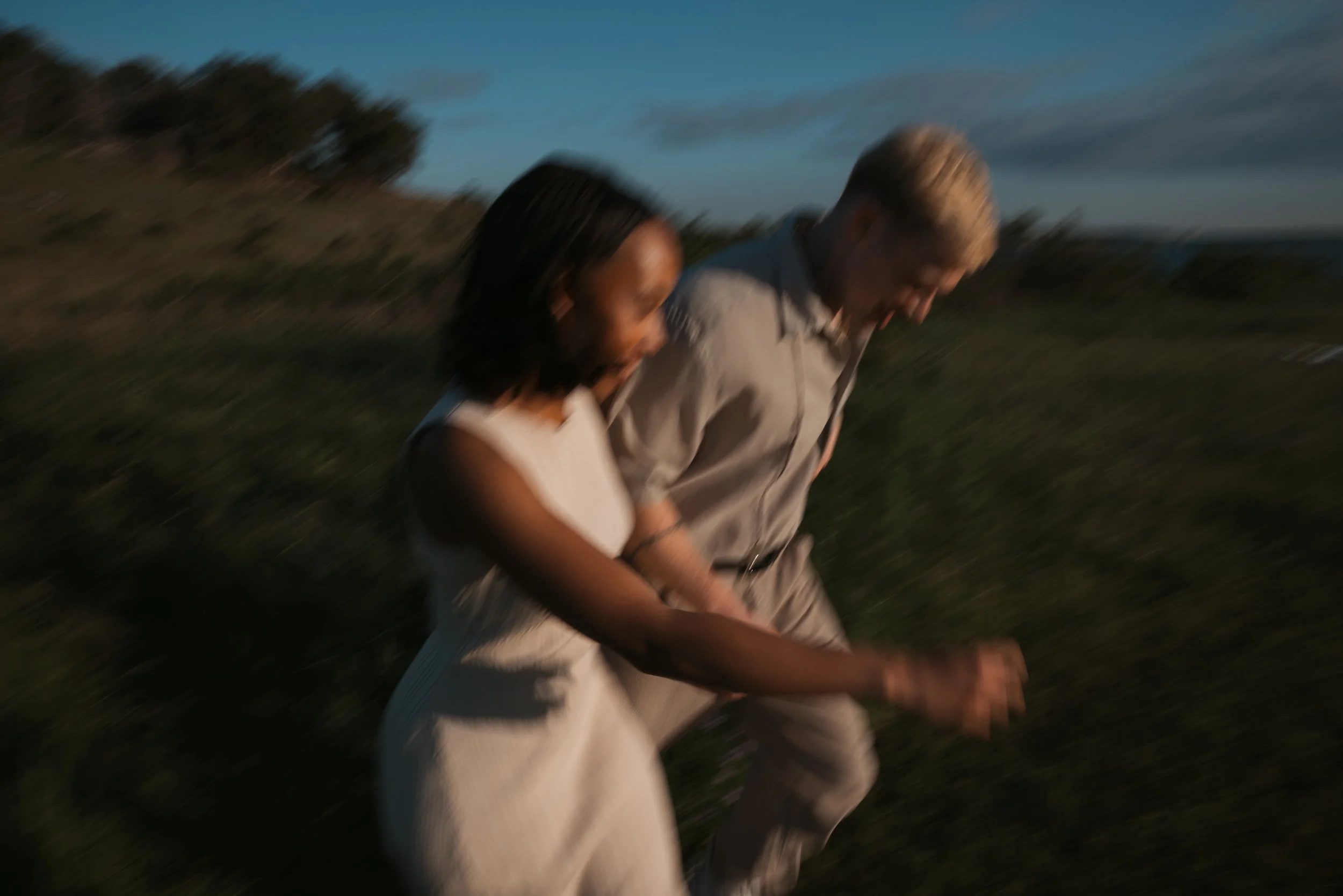 Two people walking or running in a field during dusk or early evening with a blurred background.