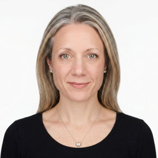 Portrait of a woman with blonde hair wearing a black top and small earrings, smiling at the camera against a white background.