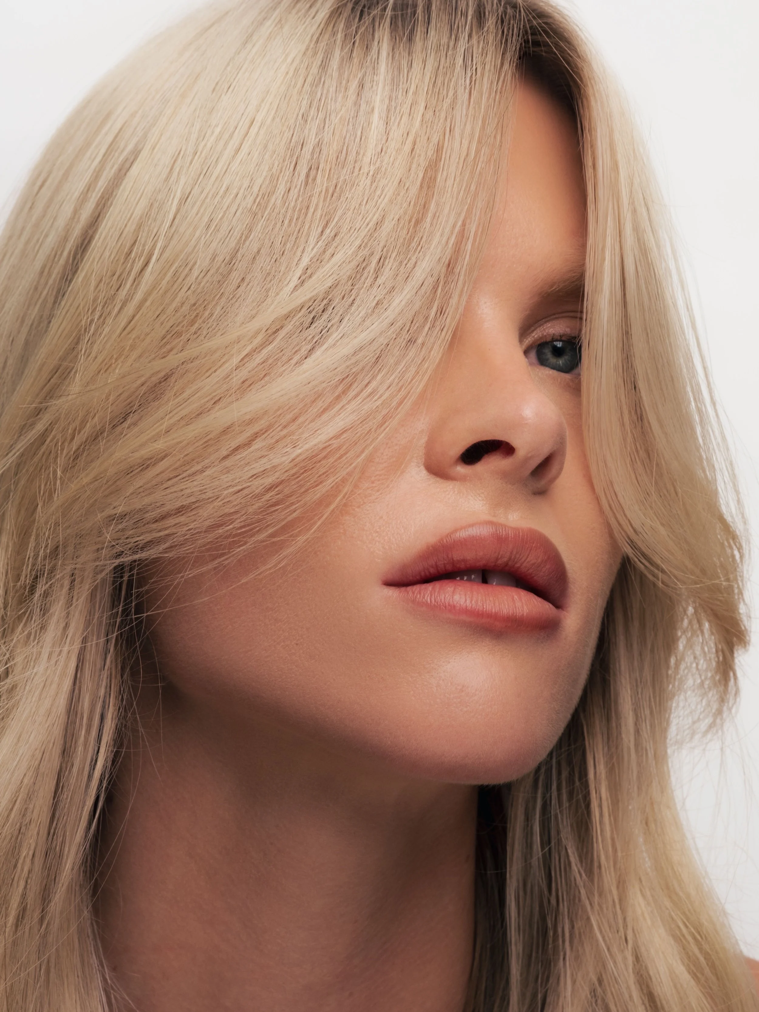 Beauty portrait of a blonde model with hair falling across her face, soft glowing makeup by Los Angeles editorial artist Amber Rose.