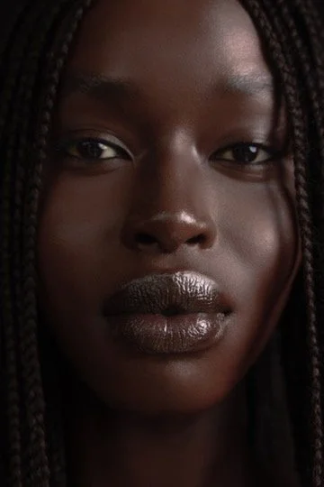 Close-up portrait of a young woman with braided hair and dark skin. Hair and makeup by Amber Rose.