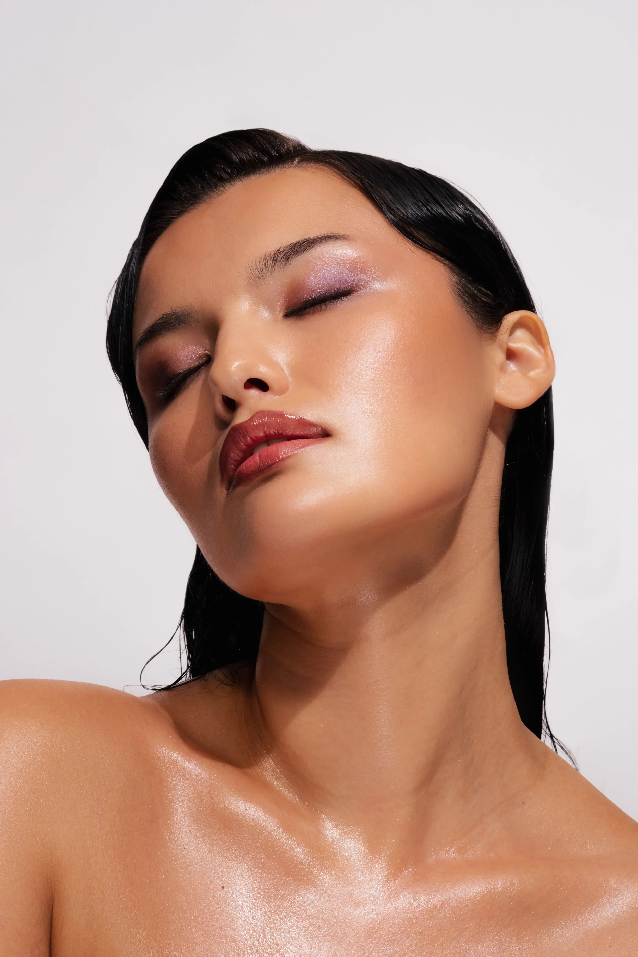 Close-up of a woman with her eyes closed and skin glowing. Hair and makeup by Amber Rose.