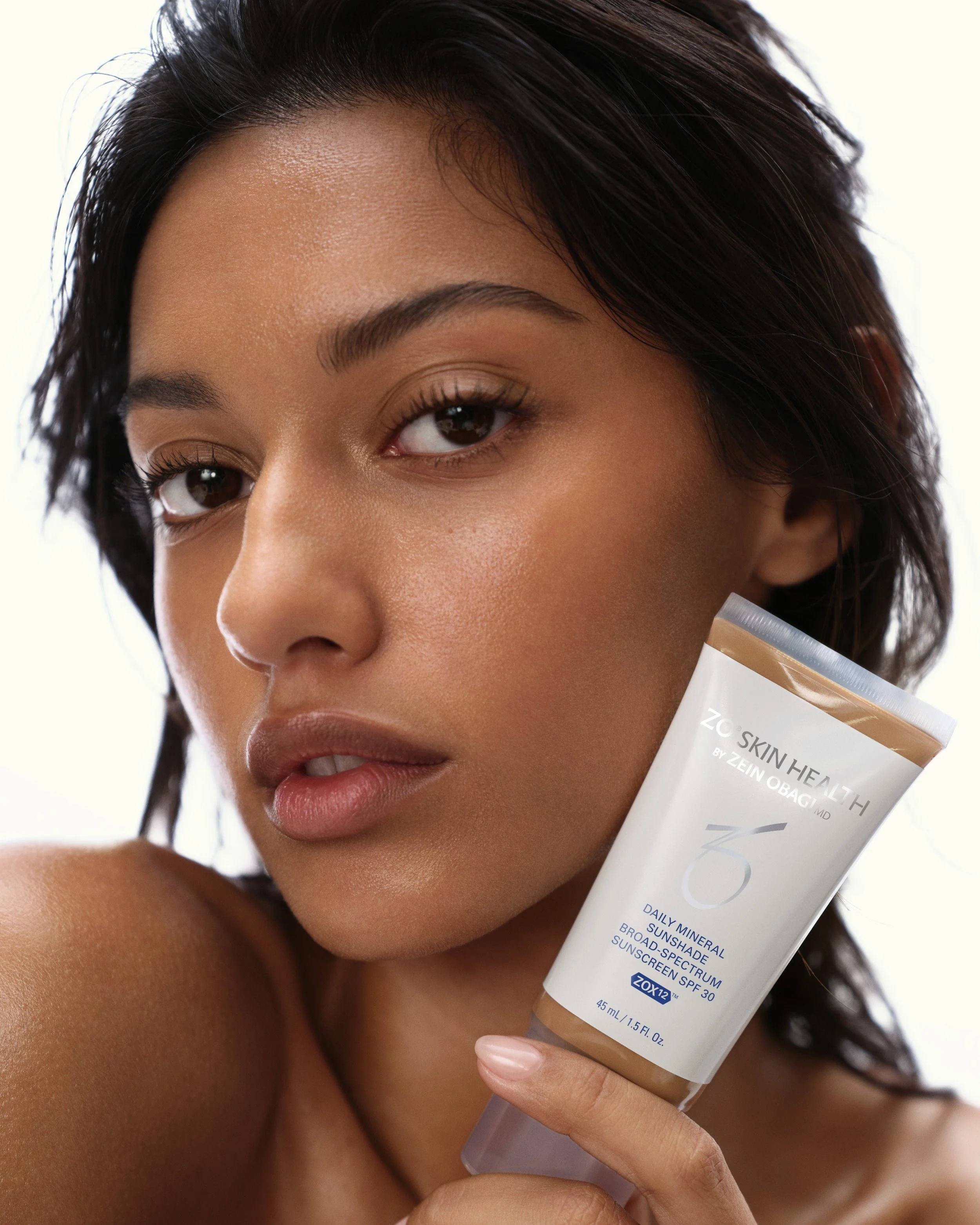 Model with glowing skin holding ZO Skin Health Daily Mineral Sunshade SPF 30. Hair and makeup by Amber Rose.