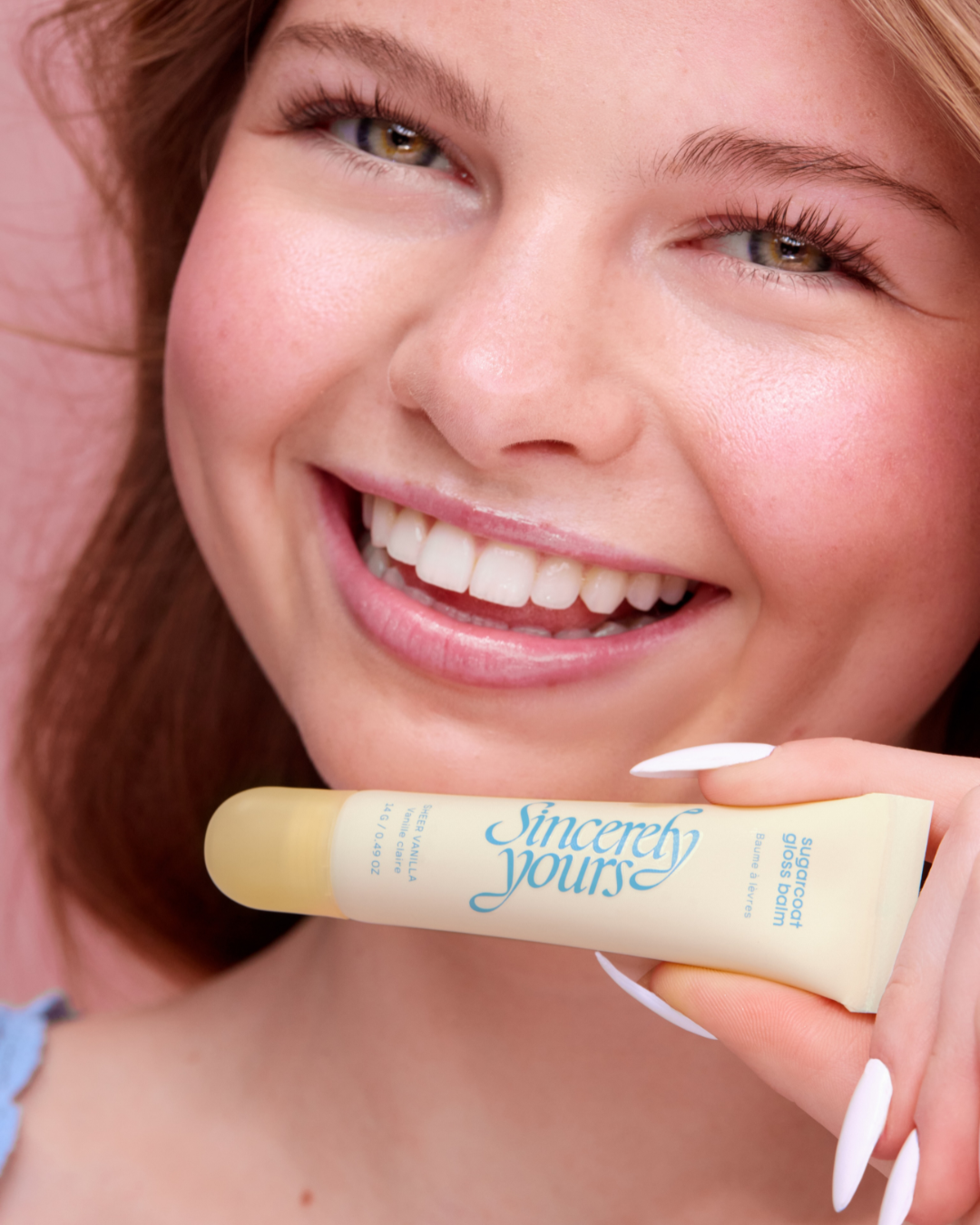 A woman with red hair smiling and holding a tube of Sincerely Yours lip balm near her lips.