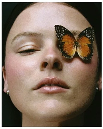 Whimsical editorial beauty portrait with a live butterfly resting on the model's cheek, soft dewy makeup by Los Angeles artist Amber Rose.