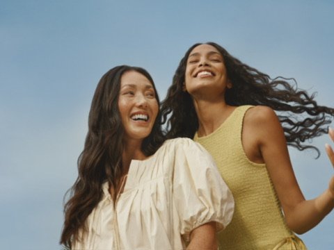 Two women smiling and enjoying outdoors under a clear blue sky.