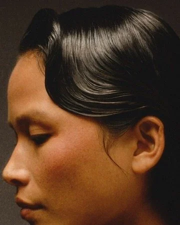Side profile of a woman with shiny black hair styled smoothly, featuring a wave detail. Hair and makeup by Amber Rose.