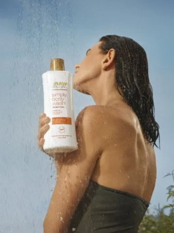 Woman holding a bottle of Raw Simply Body Wash in the shower with water splashing.
