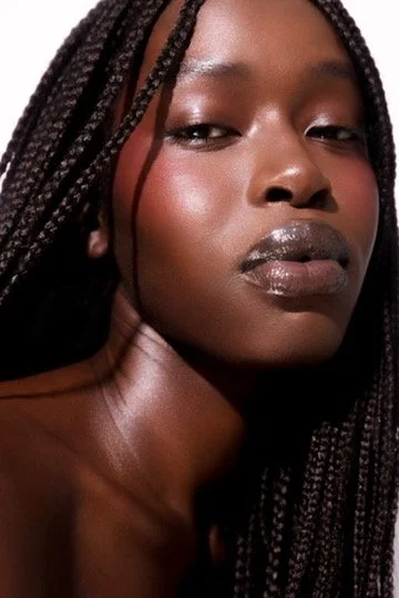 Close-up portrait of a woman with braided hair and glossy lips looking confidently at the camera. Hair and makeup by Amber Rose.