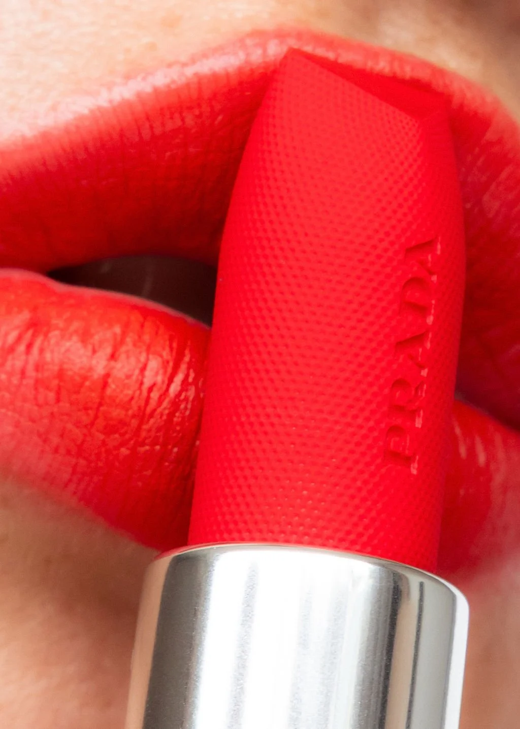 Close-up of a person applying bright red lipstick to their lips, holding a red lipstick tube. Hair and makeup by Amber Rose.